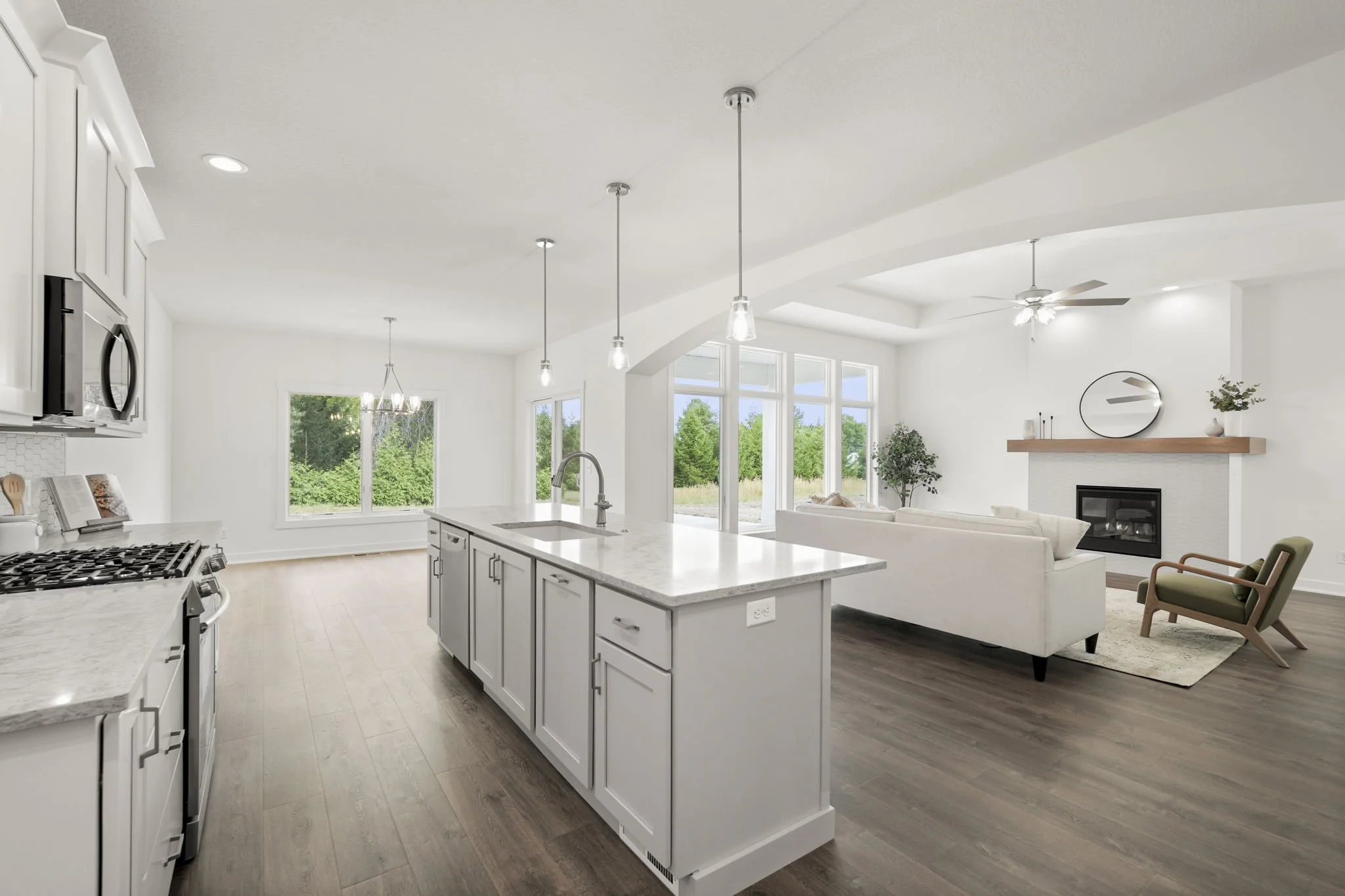 Open-concept kitchen and living room with white cabinets, island, hardwood floors, large windows, and modern decor.