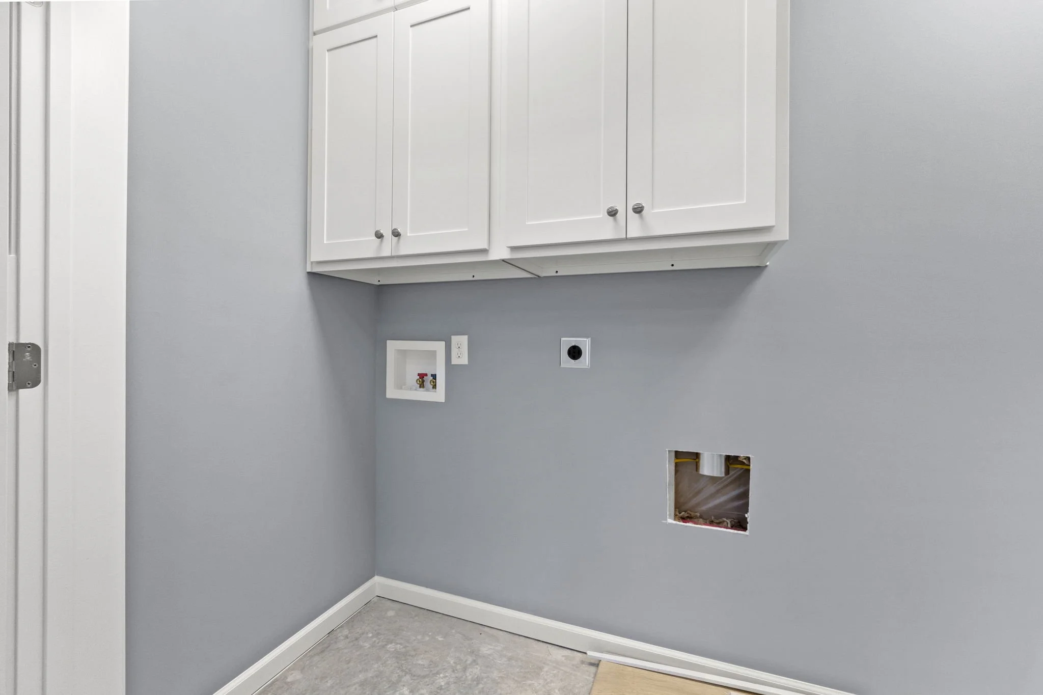 Empty laundry room with white cabinets, gray walls, and electrical and plumbing hookups for washer and dryer.