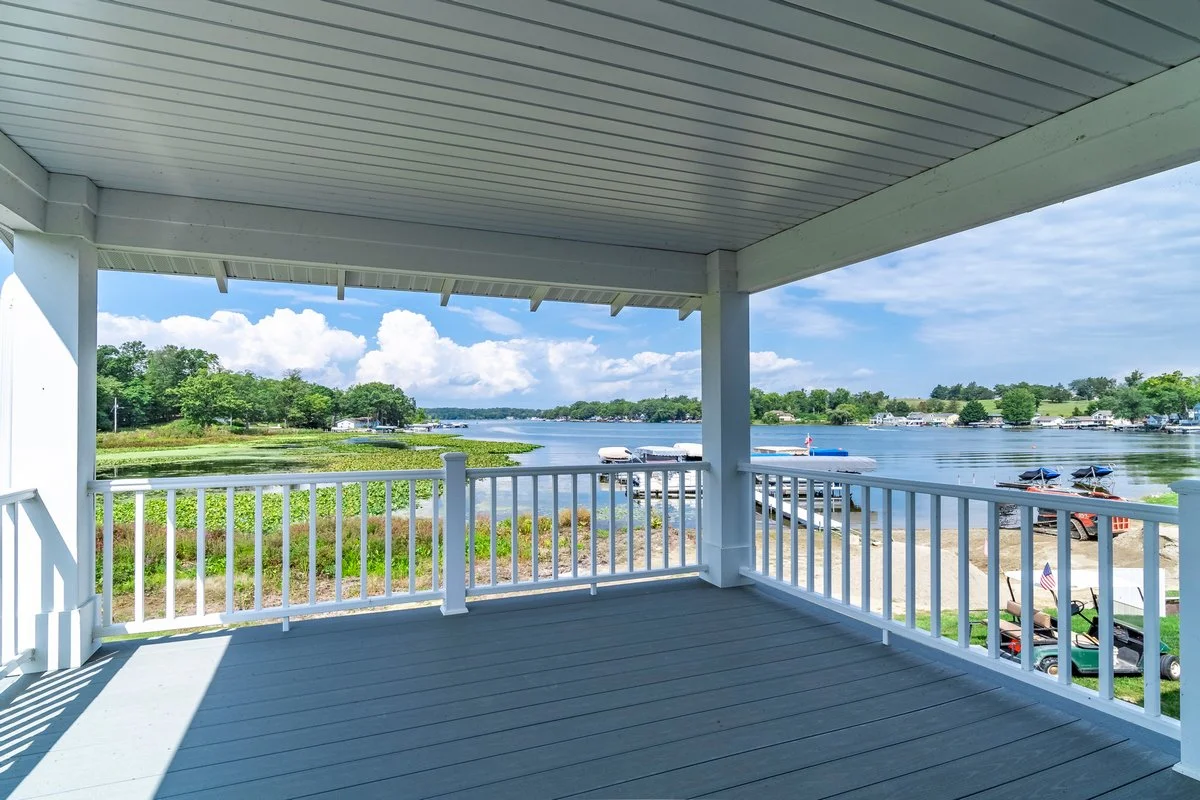 View of a river with boats and houses in the distance, taken from a covered balcony with white railing and ceiling