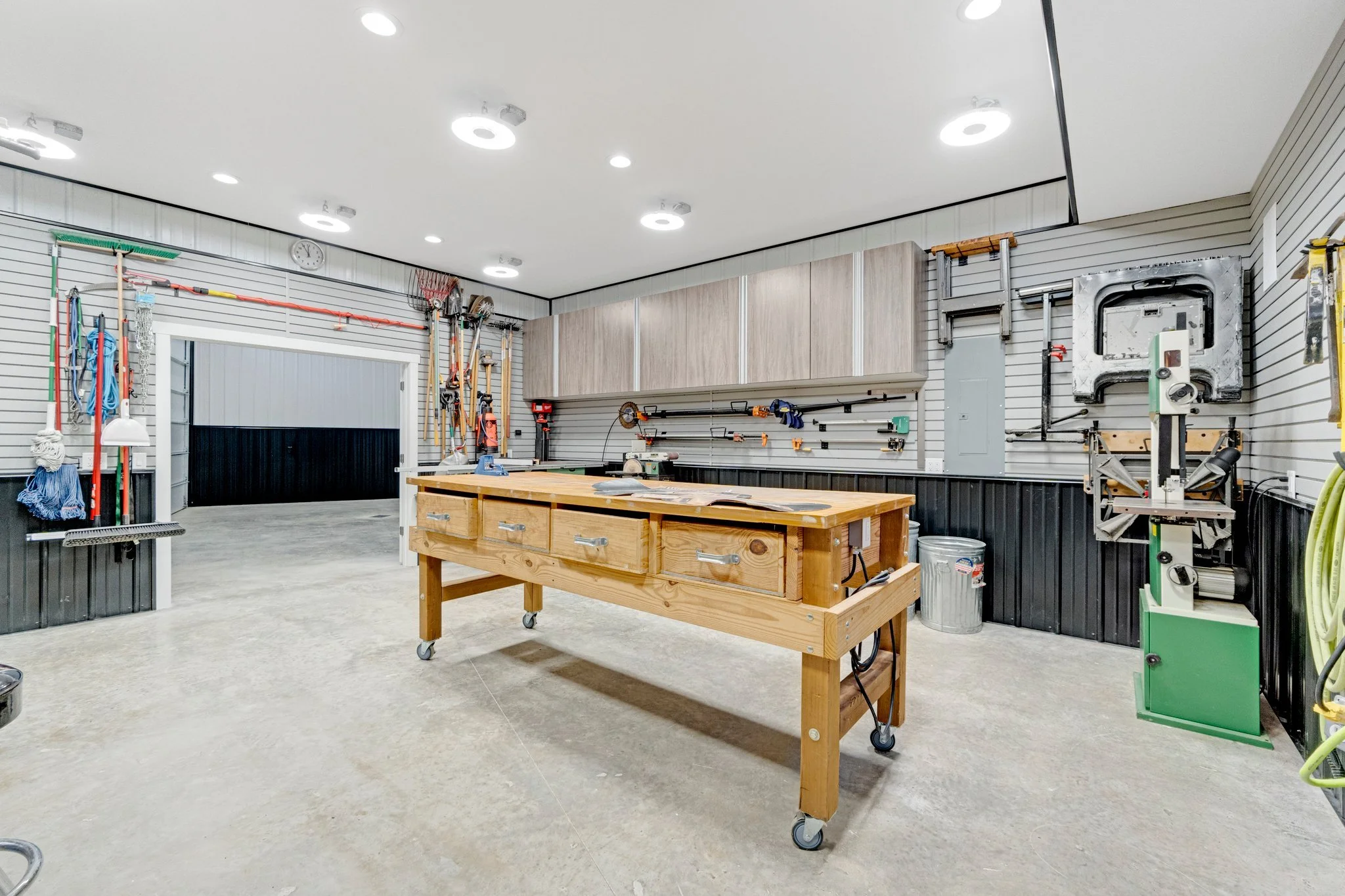 A well-organized outdoor workshop with various tools mounted on slat walls, a large work table, and bright overhead lighting.