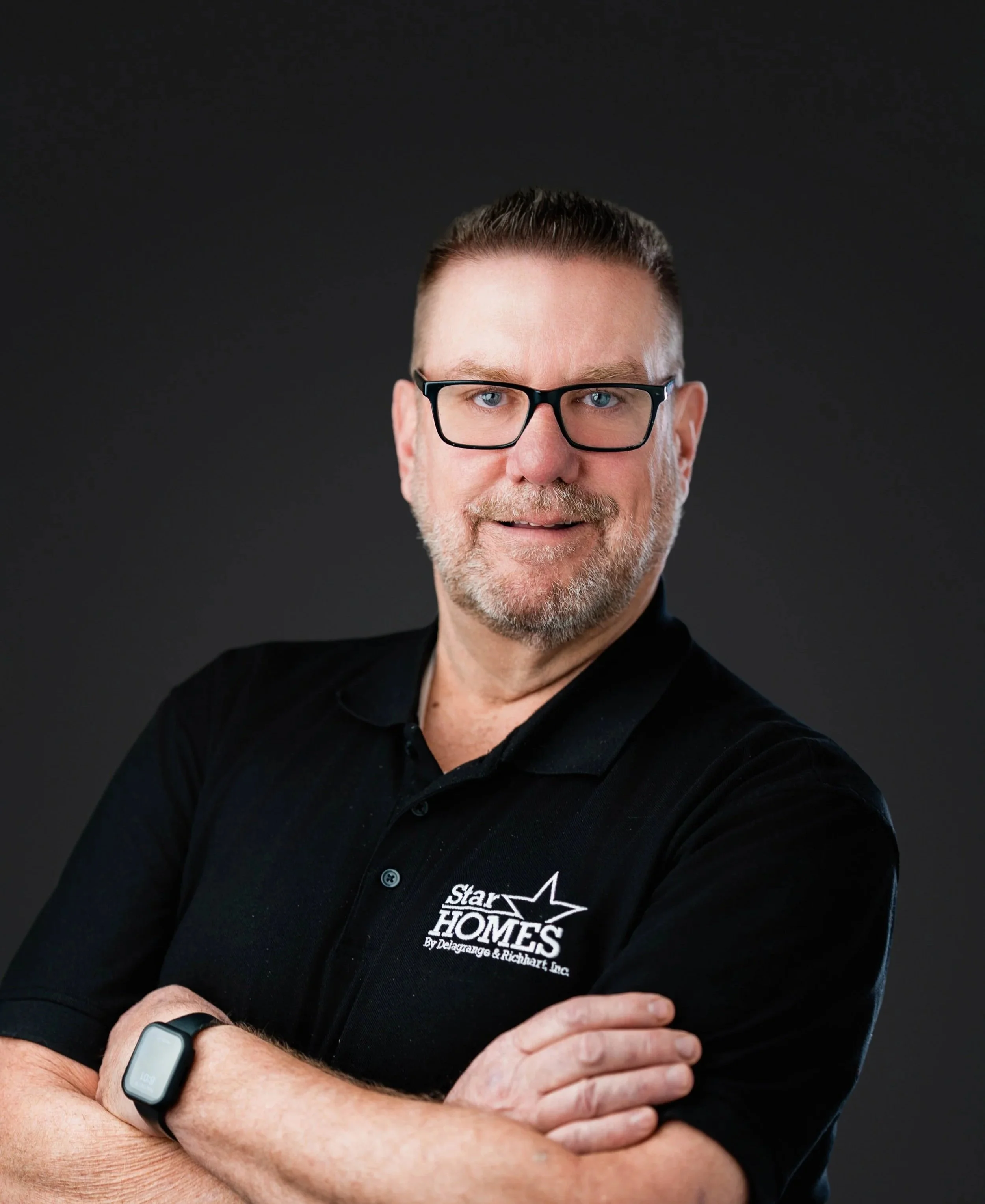 A middle-aged man with glasses, short brown hair, and a beard, wearing a black shirt with a logo that reads 'Star Homes,' standing against a black background.