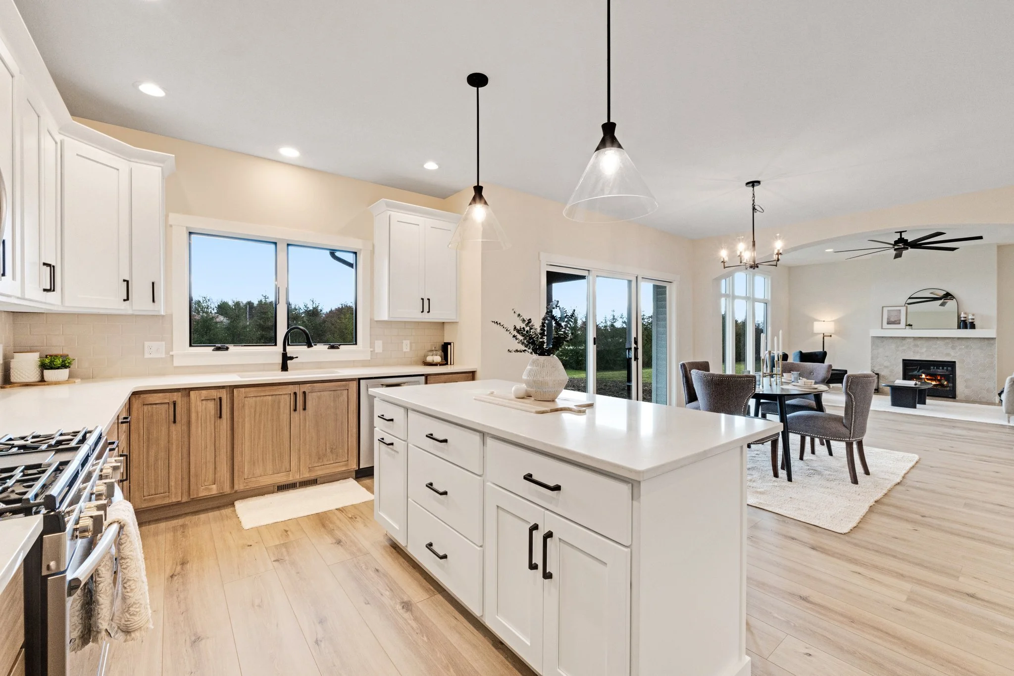 Open-concept kitchen and living room with white cabinets, wood accents, dining area, and cozy fireplace.