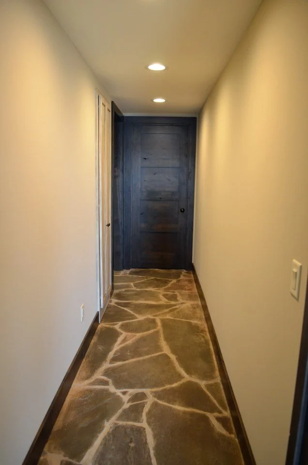 Narrow hallway with cream-colored walls, a stone-patterned floor, and a dark blue door at the end.