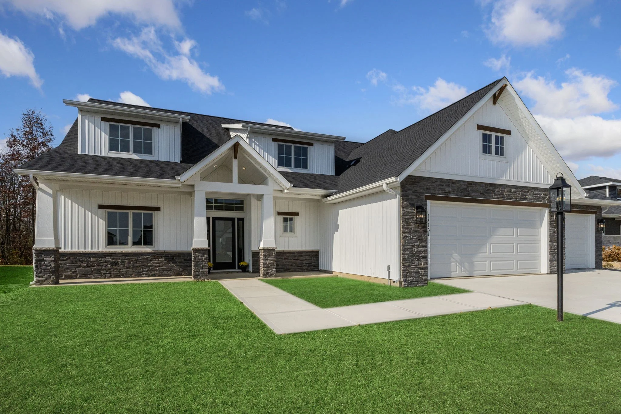 Modern two-story house with a black roof, white and stone exterior, front door, three garage doors, and some landscaping.