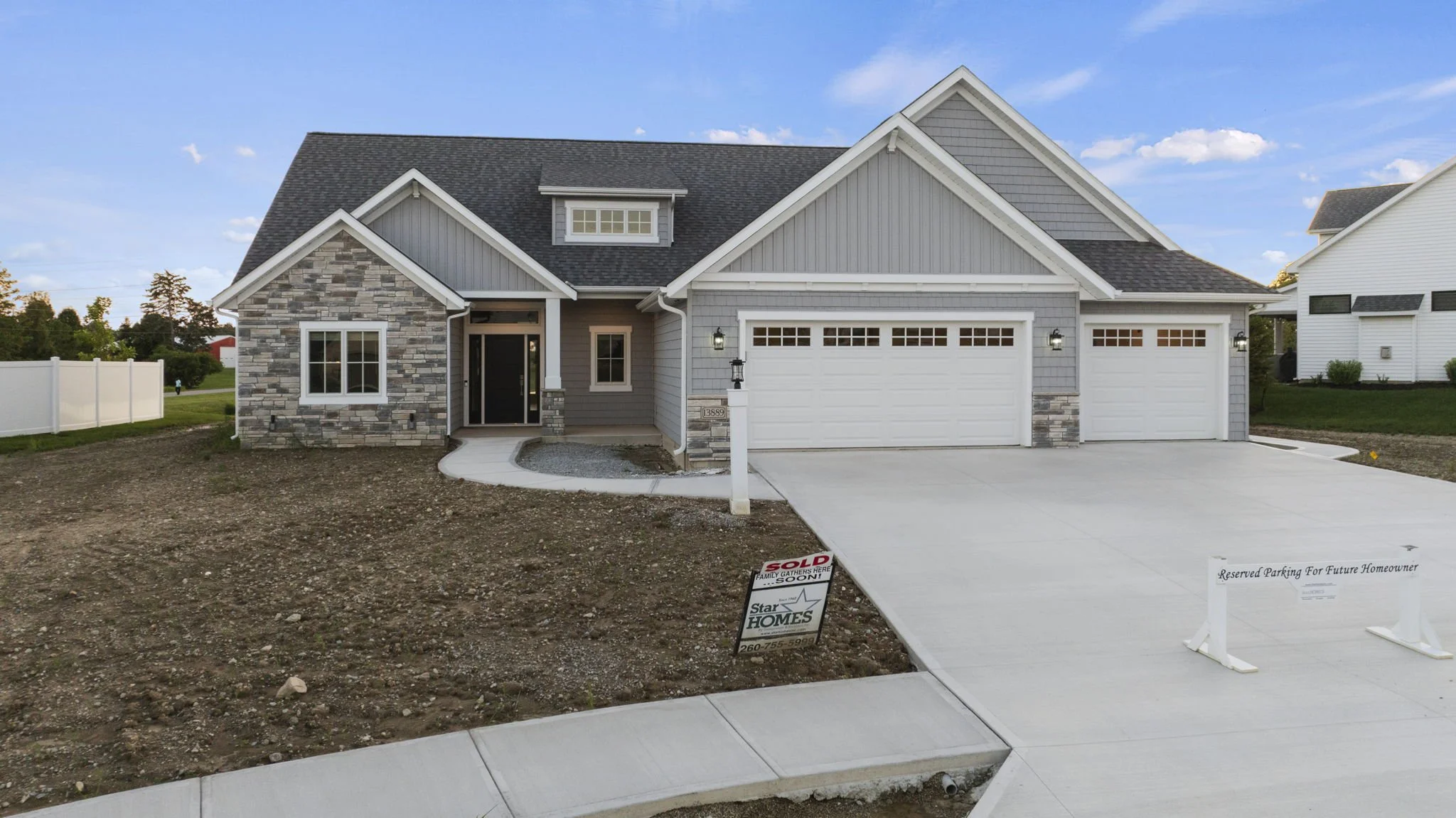 Newly built house with gray siding and stone accents, white garage doors, a concrete driveway, and a lawn area under construction.