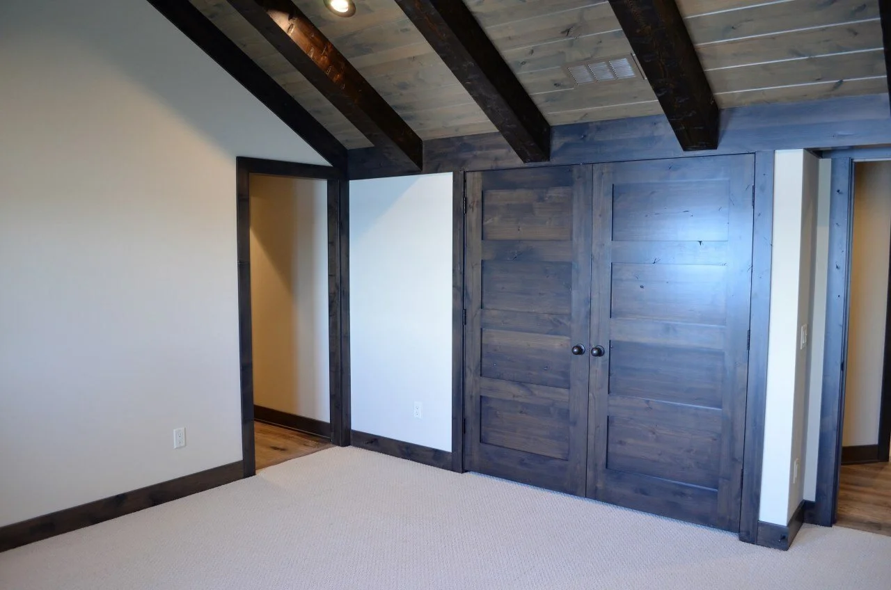 Empty room with dark wooden beams, closet with sliding doors, and beige carpet.