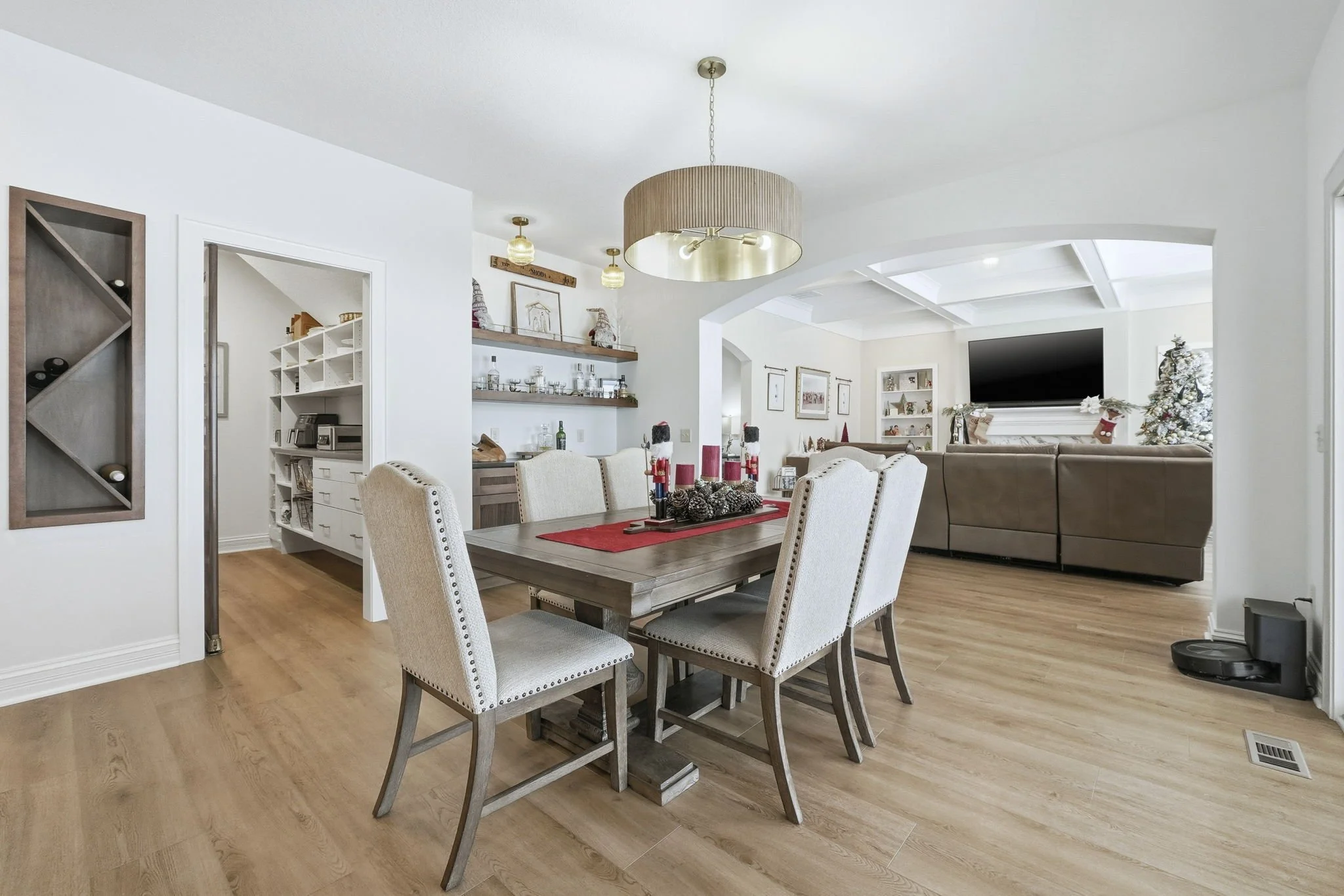 Open concept living and dining room with wooden flooring, a wooden dining table with six beige upholstered chairs, a beige sectional sofa, a large flat-screen TV, and a decorated Christmas tree.