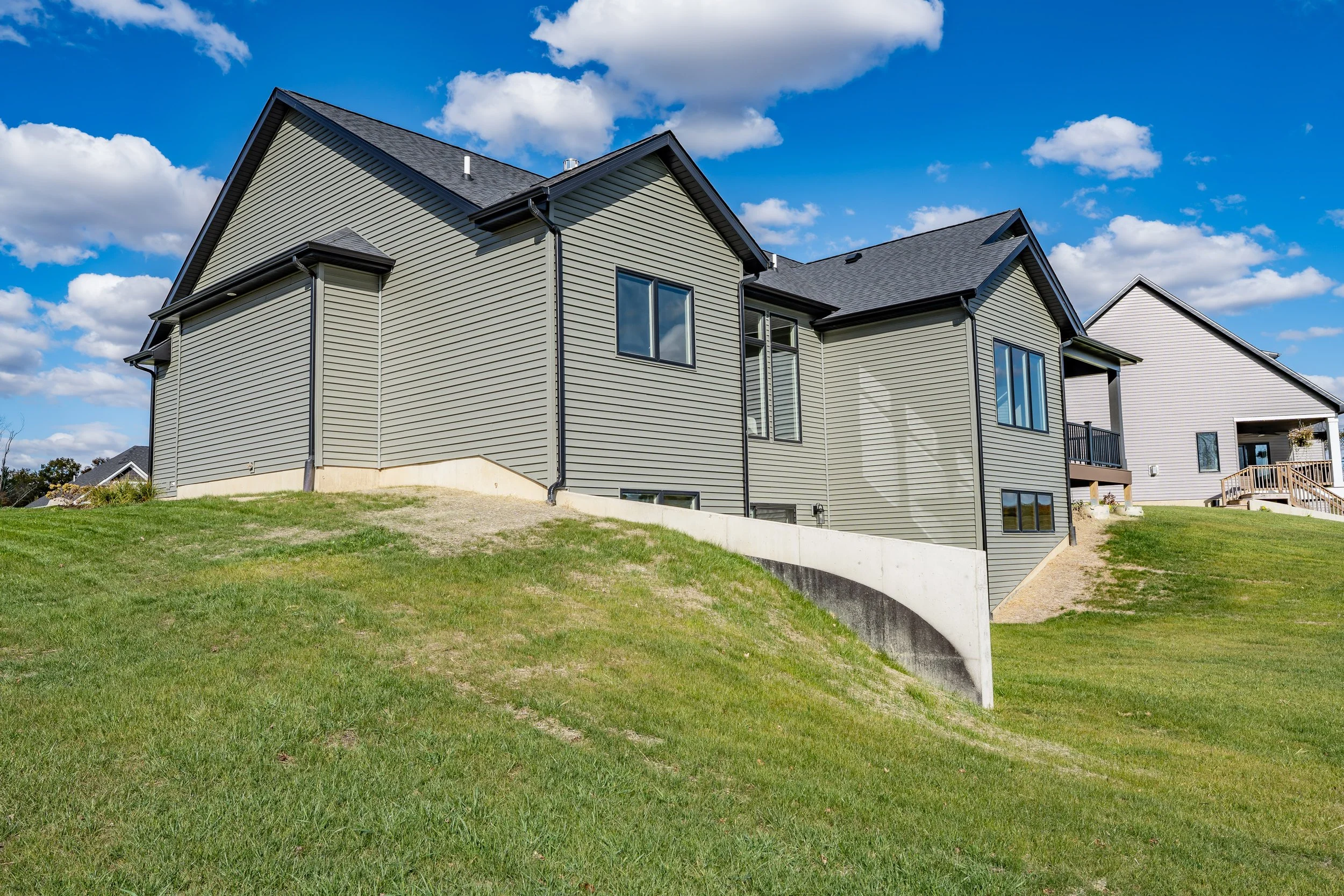 Side view of a modern house on a grassy hill under a partly cloudy sky.
