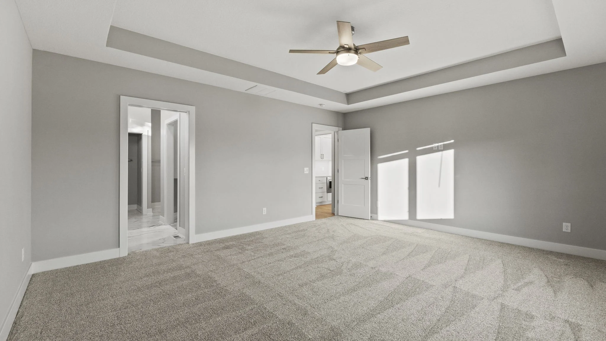 Empty bedroom with beige carpet, gray walls, ceiling fan, and sunlight streaming through window.