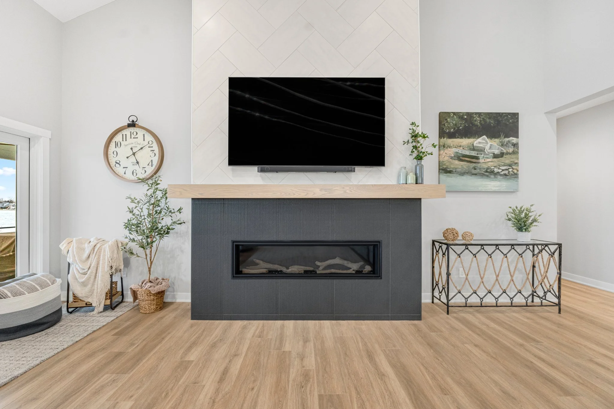 Living room with a fireplace, wall-mounted TV, clock, plants, artwork, and a metal table.