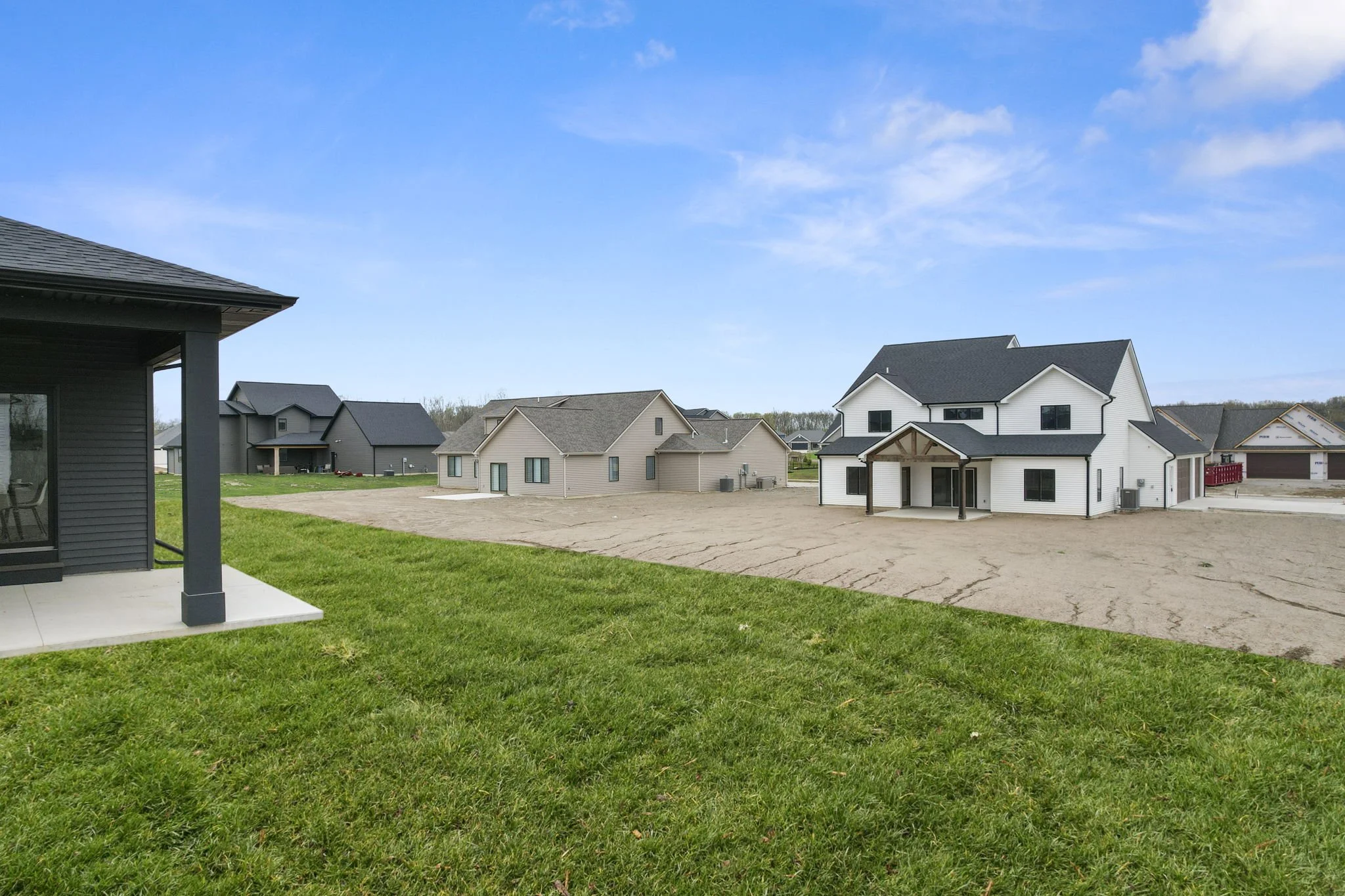 Residential neighborhood under construction with several houses, some finished and some in progress, and a grassy area and dirt lot in the foreground.