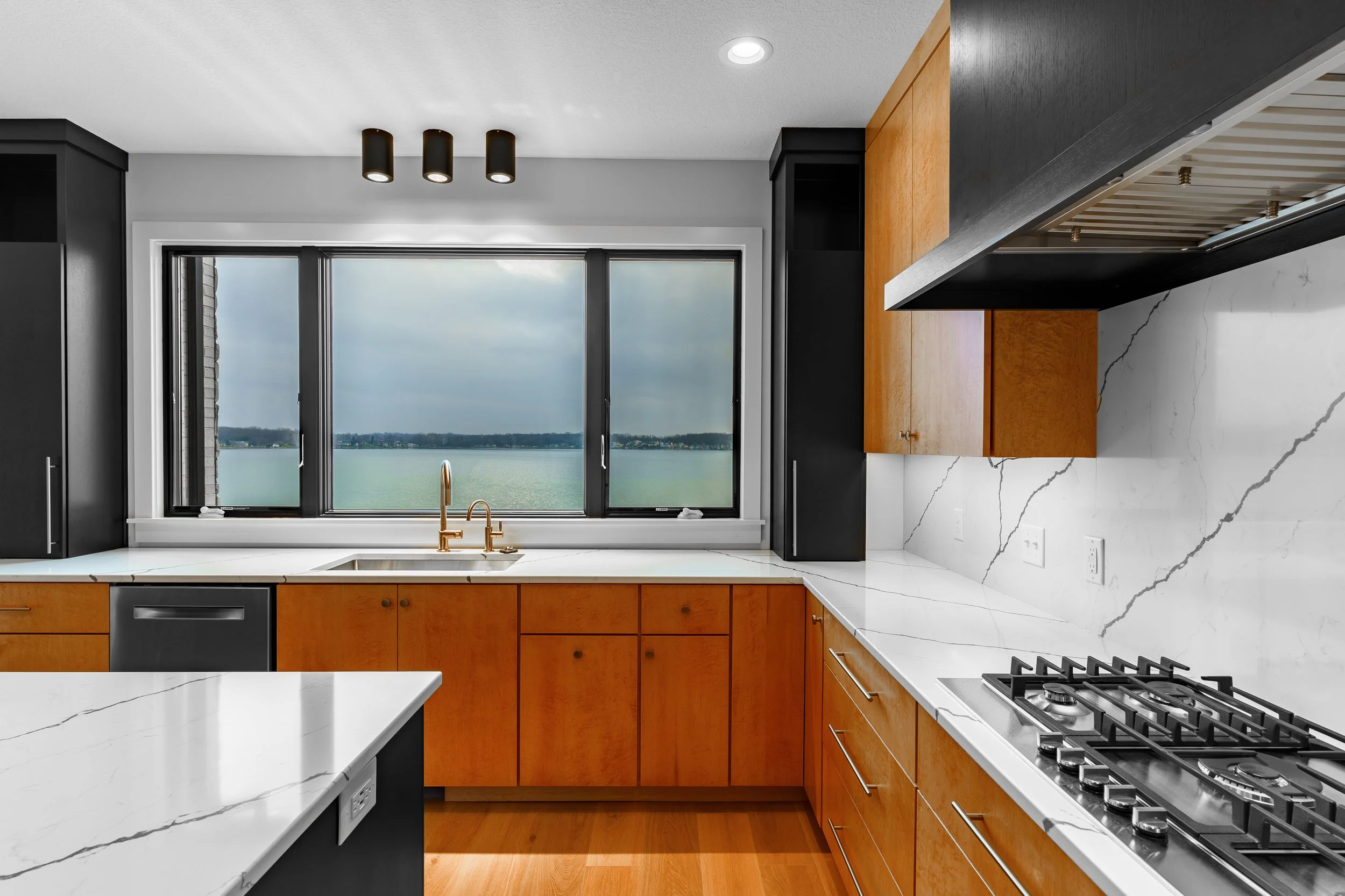 Modern kitchen with wooden cabinets, white marble countertops, a window overlooking a body of water, and a gas stove.