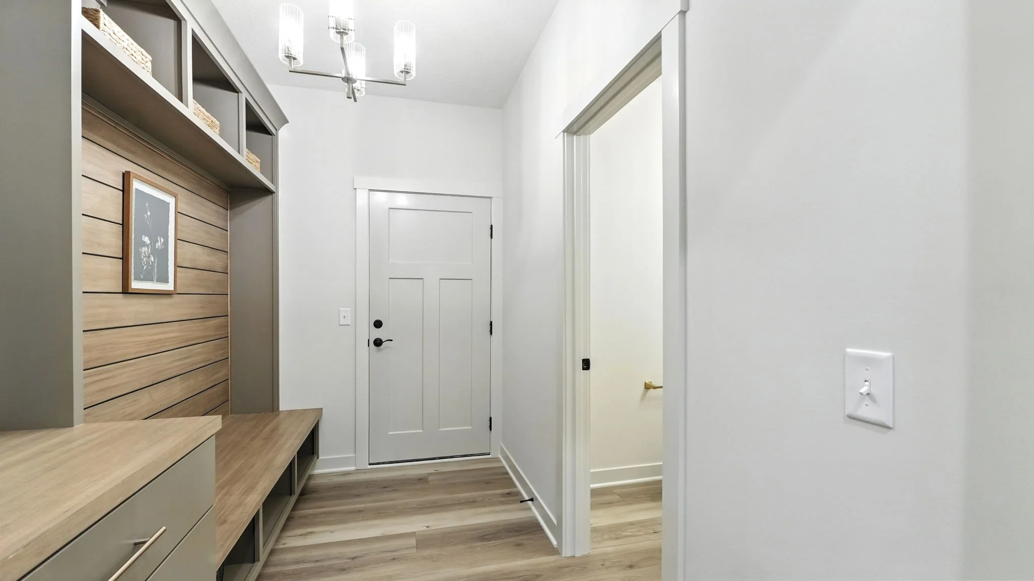 Foyer with white door, wood flooring, and built-in gray and wood storage unit on the left, with a chandelier overhead.