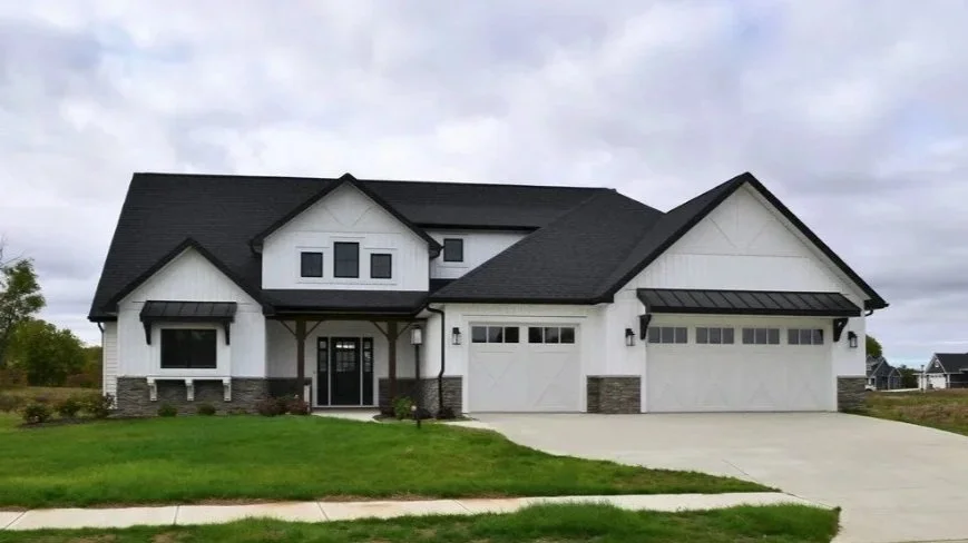 Modern white house with dark roof, front yard, driveway, and garage doors