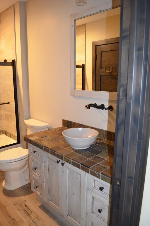 Bathroom vanity with a vessel sink, mirror, bathroom mirror, toilet, shower with glass door, and wood flooring.