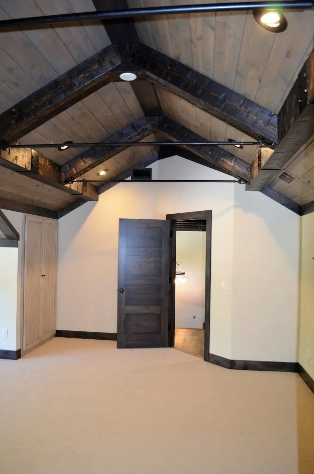 Interior of a room with a vaulted wooden ceiling, partially open dark wooden door, a built-in closet, beige carpeted floor, and white walls.