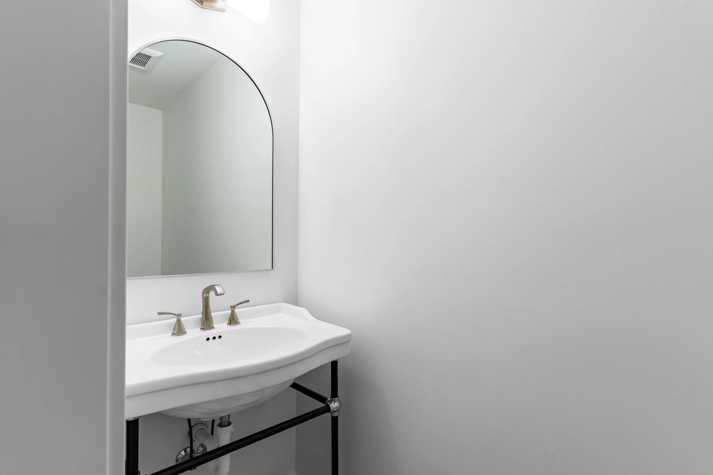 Bathroom with a white sink, silver faucet, and a large mirror on a plain gray wall.