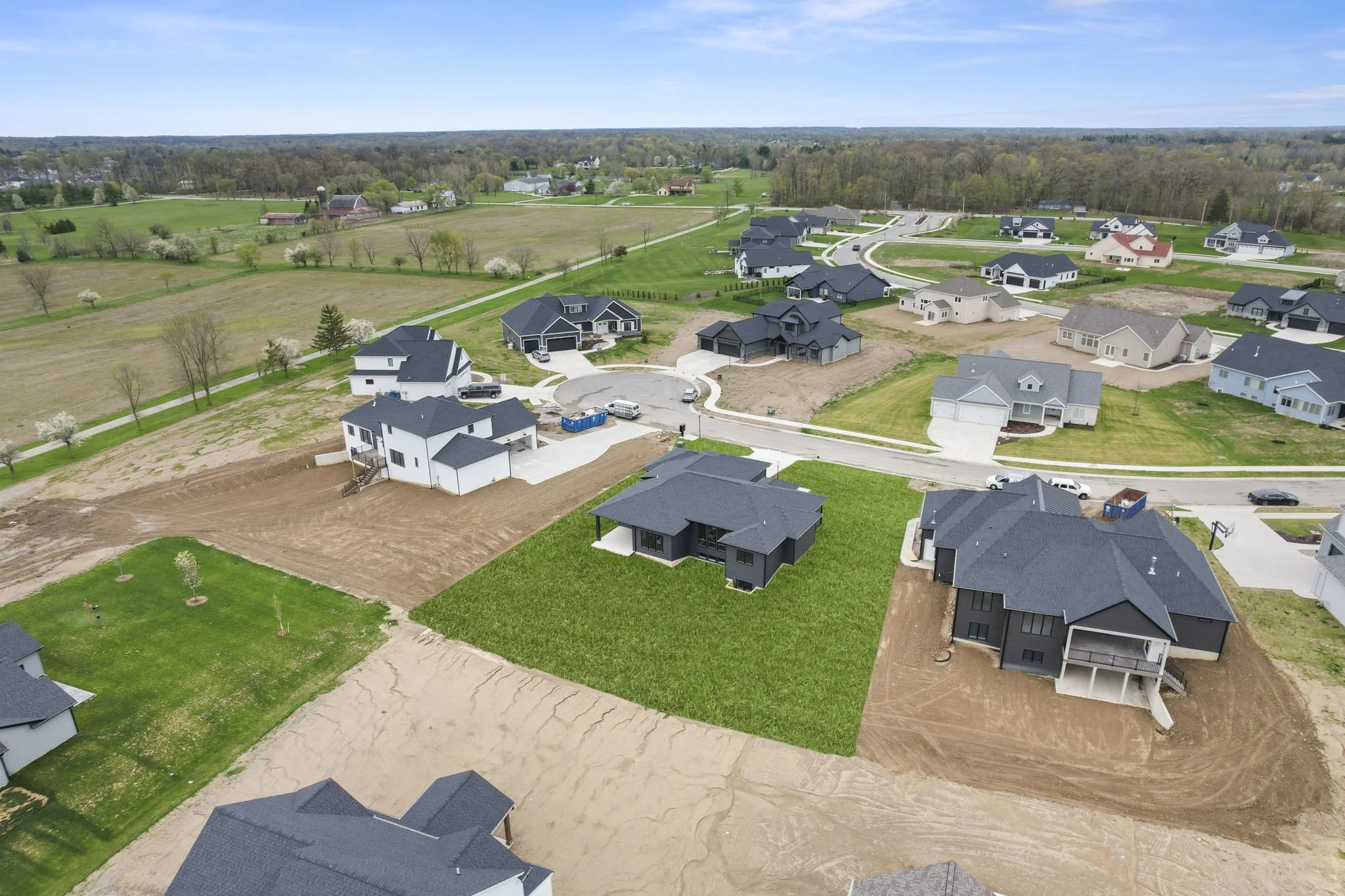 Aerial view of a residential neighborhood with several houses under construction, including partly built houses with construction materials, green lawns, and surrounding trees.