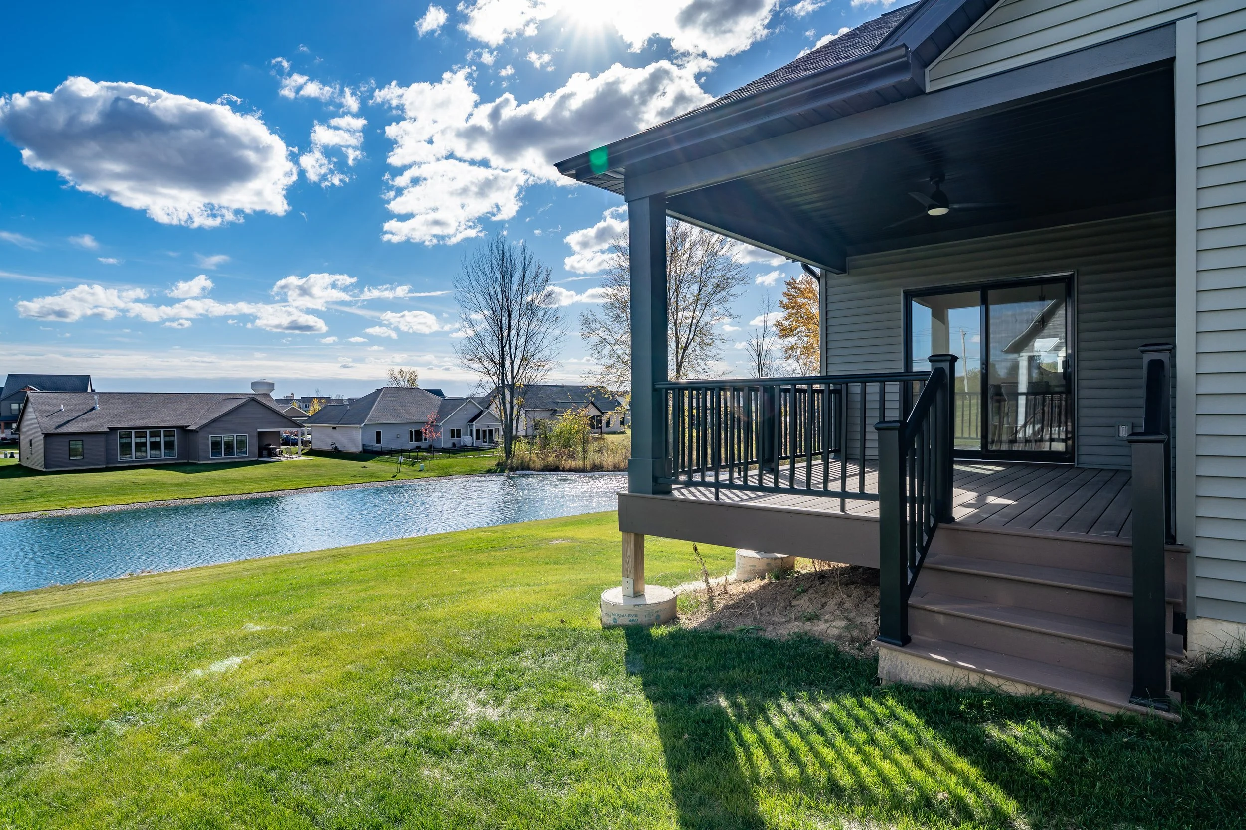 View from a house balcony overlooking a pond and neighboring houses under a partly cloudy sky.