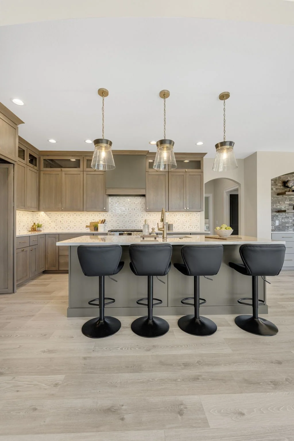 Modern kitchen with gray cabinetry, a kitchen island with four black barstools, pendant lights, and a light wood floor.