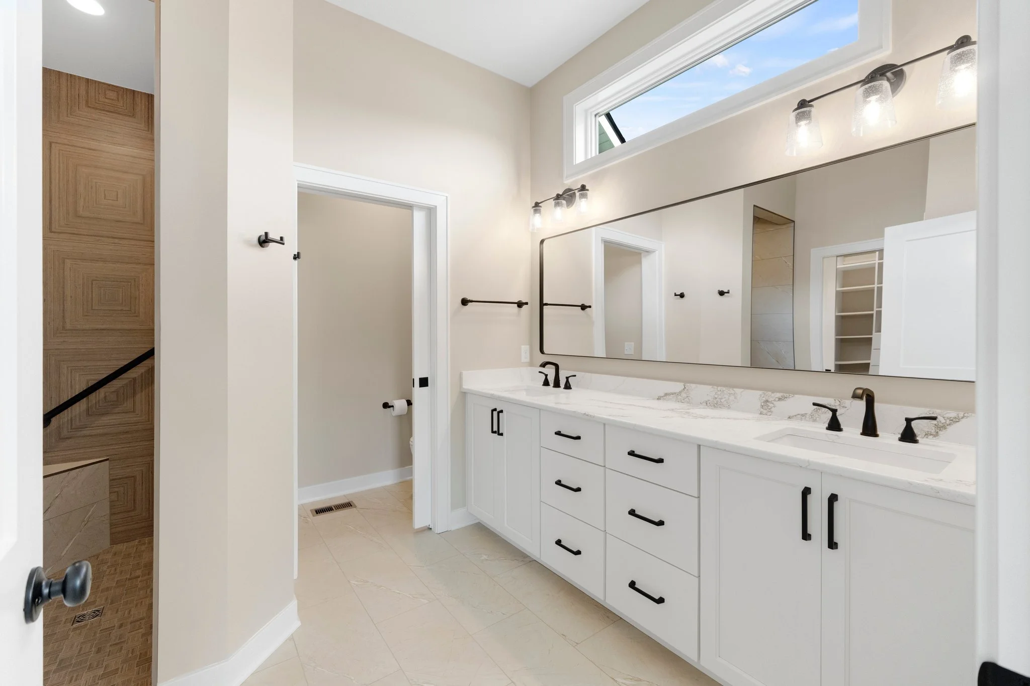 Bathroom with double white vanity, black fixtures, large mirror, and natural light from high window.