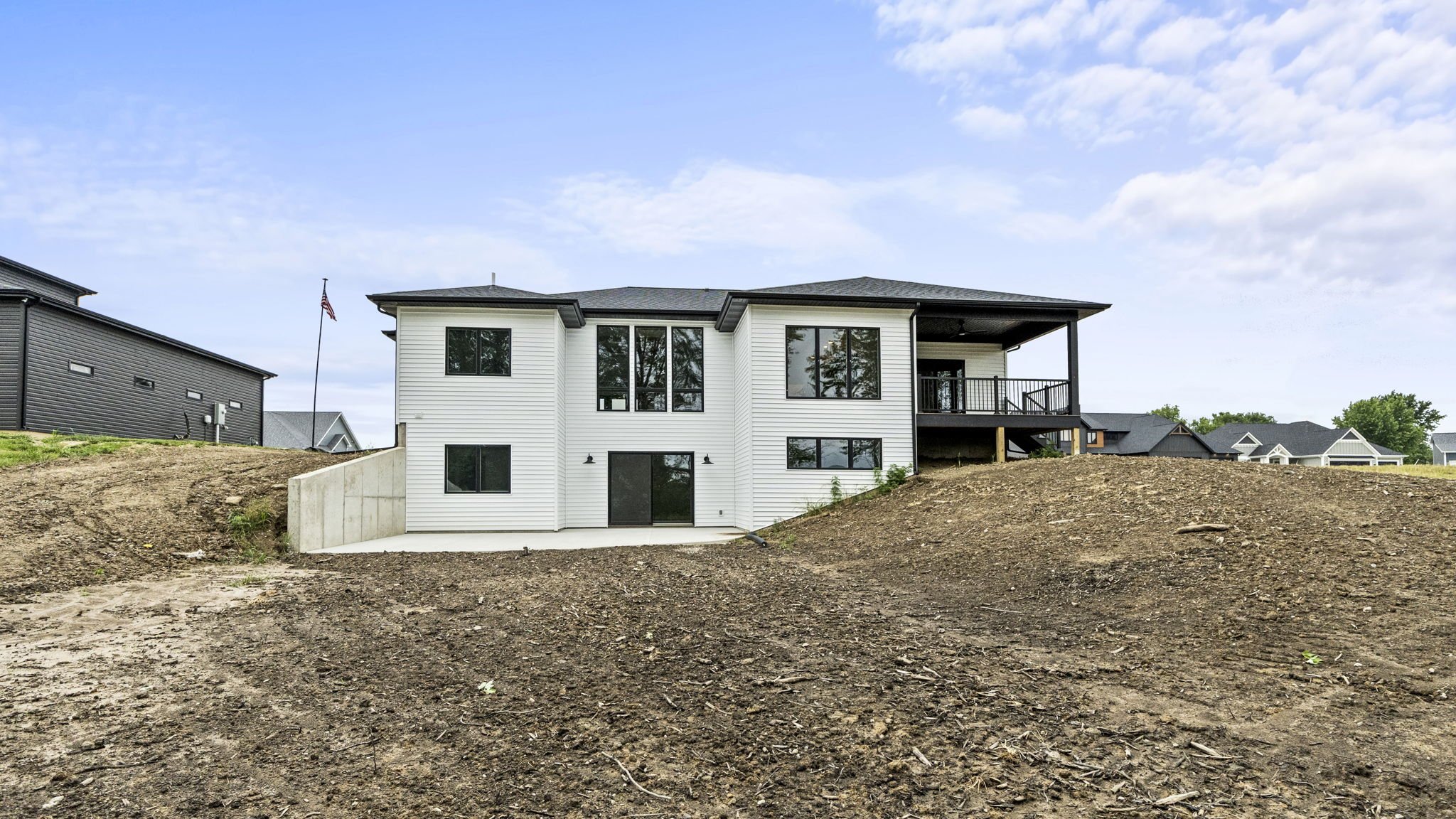 Back view of a modern two-story house with white exterior, large windows, a balcony, and a backyard with barren soil