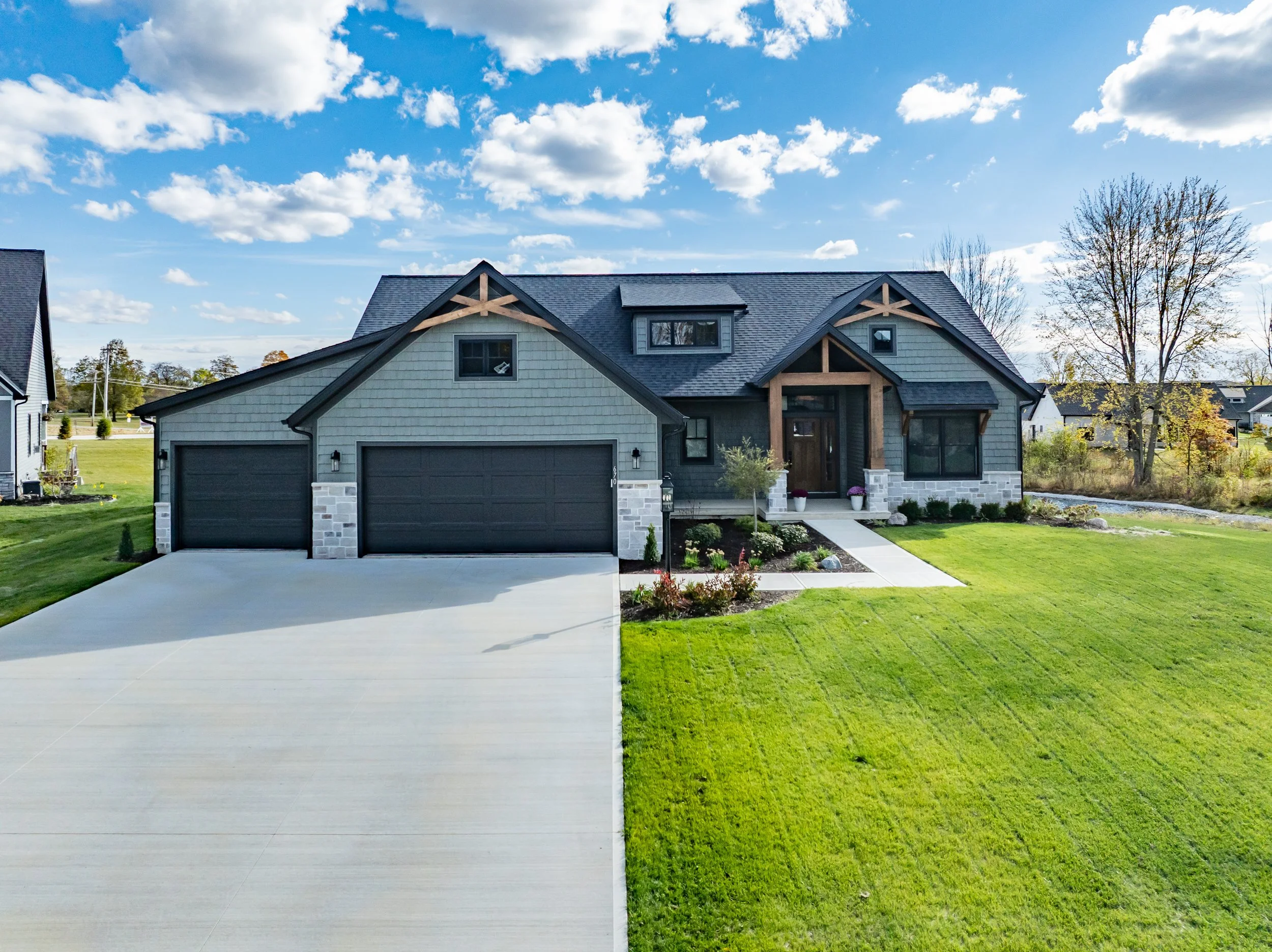 A modern two-story house with a gray exterior, black garage doors, and a front yard with green lawn and landscaping.