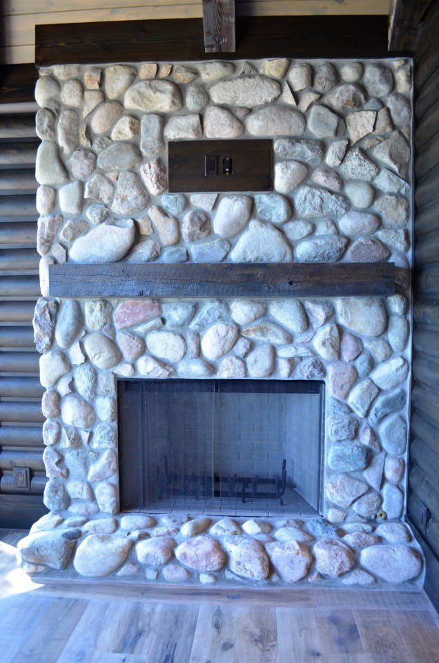 Stone fireplace with a dark brown wooden mantel and a metal mesh screen, set against wooden wall panels.