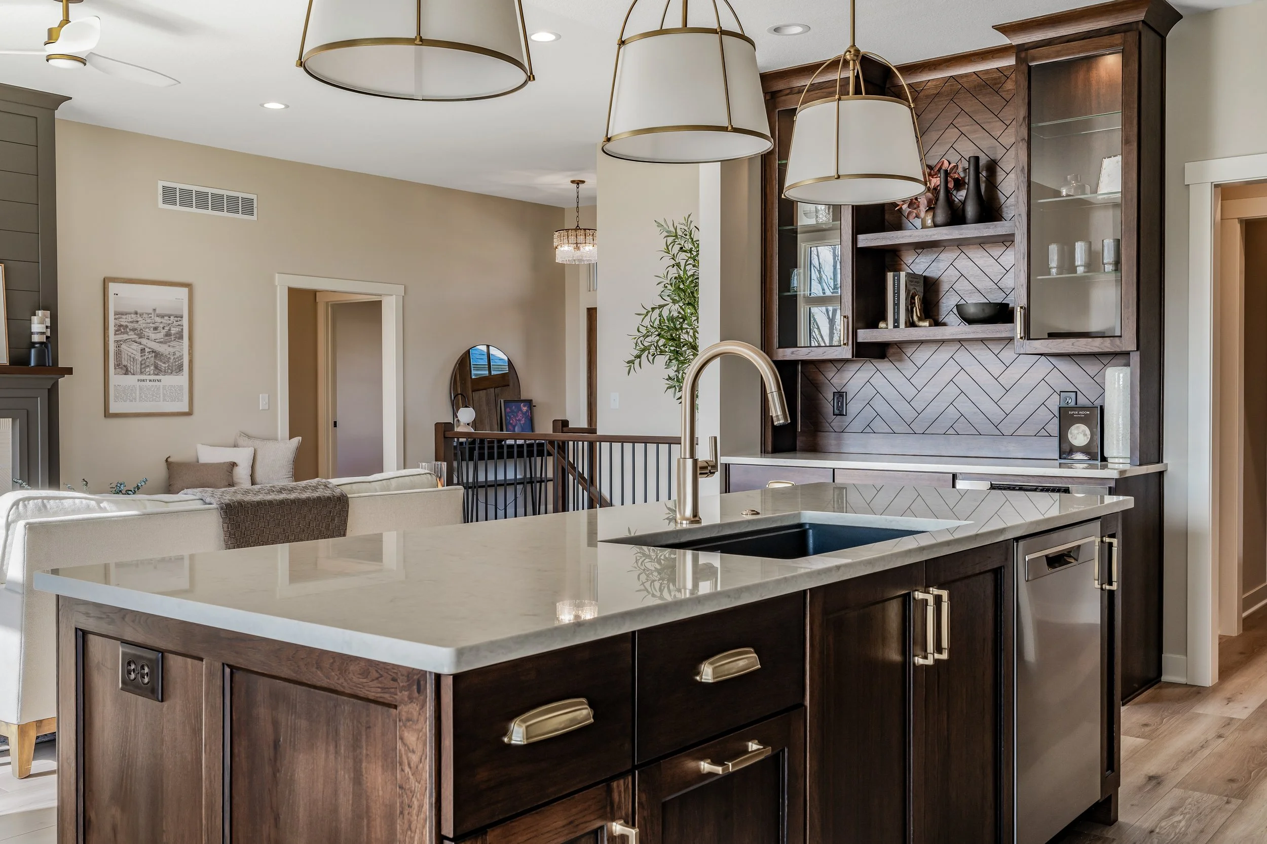 Modern open-concept kitchen with dark wood cabinetry, a white marble island, brass hardware, and pendant lighting, overlooking a dining and living area.