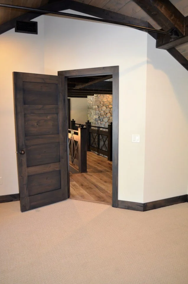 A doorway leading to a room with wooden floors and a stone wall, featuring a dark wood staircase with black metal railings.