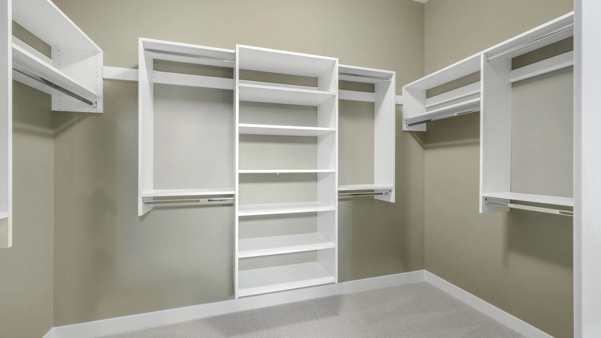 Empty walk-in closet with white shelving units, hanging rods, and beige walls.