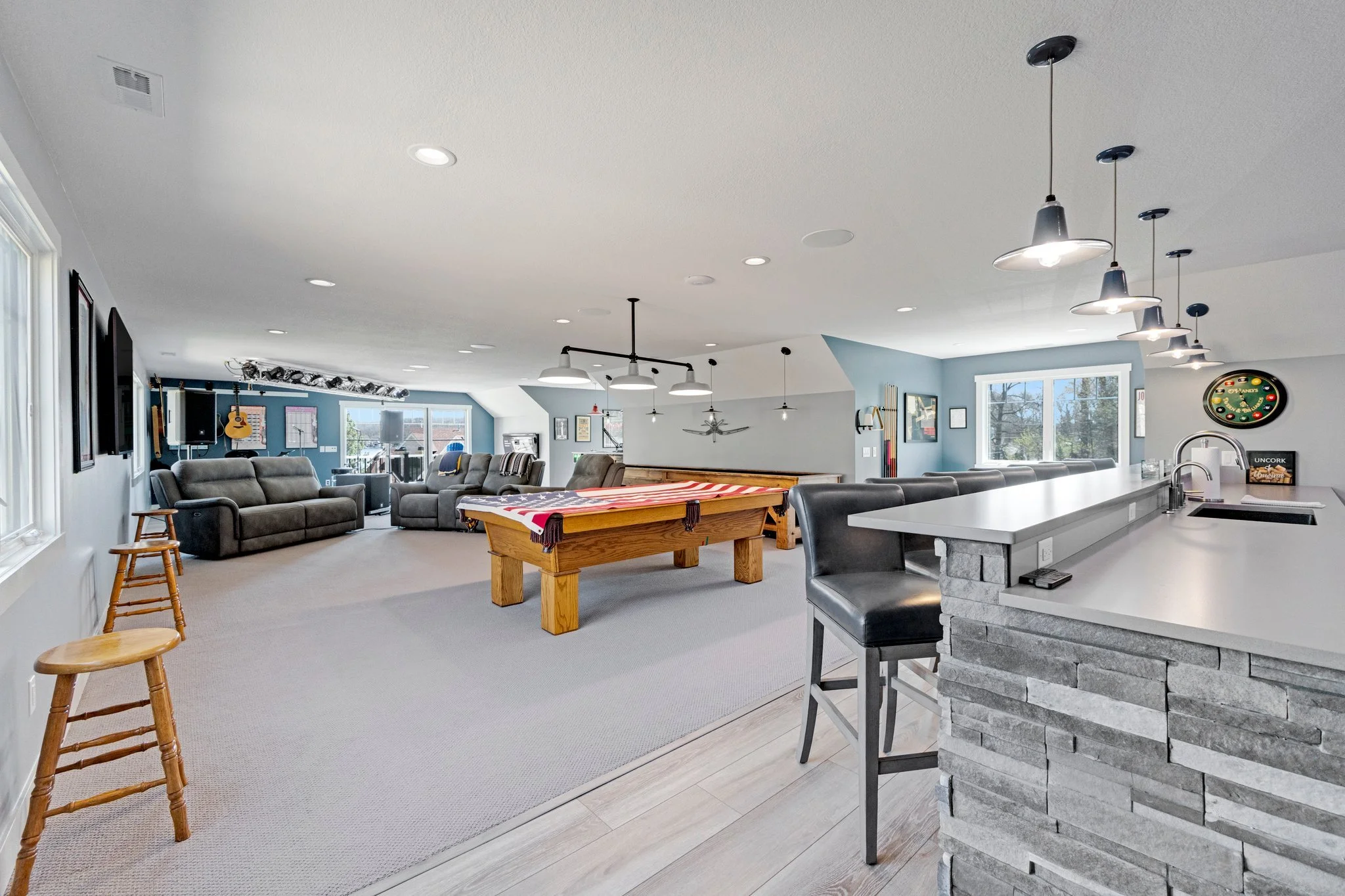 Open-concept basement game and lounge area with multiple sofas, a foosball table, a bar with black chairs, a dartboard, and musical instruments on the wall.