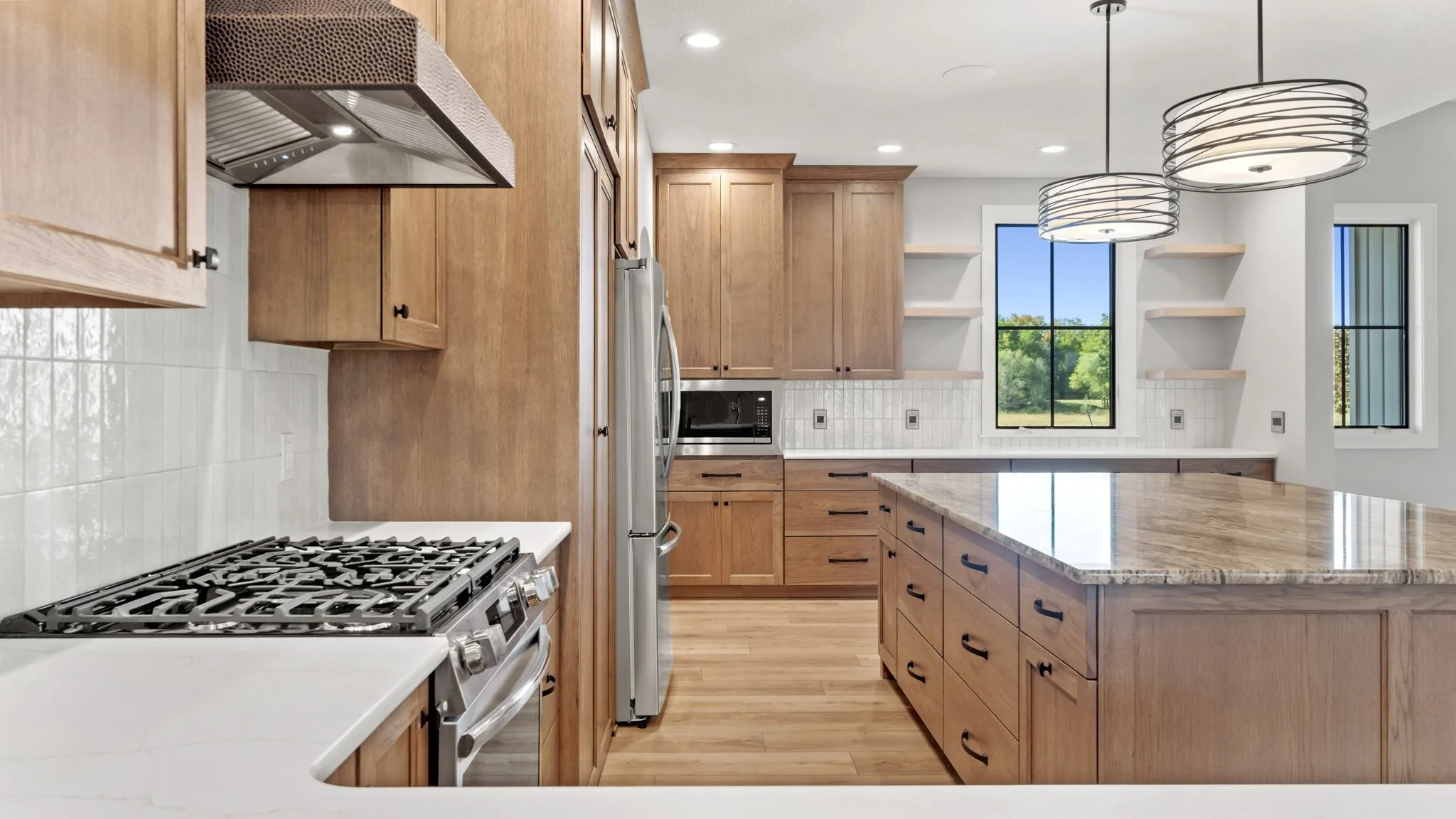 Modern kitchen with wooden cabinets, white countertops, a marble island, stainless steel appliances, and two large pendant light fixtures.