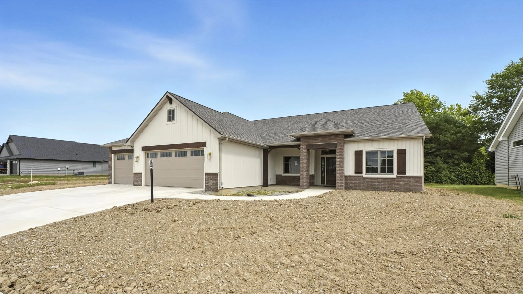 Newly constructed single-story house with a two-car garage, brick accents, and front porch under a clear blue sky.