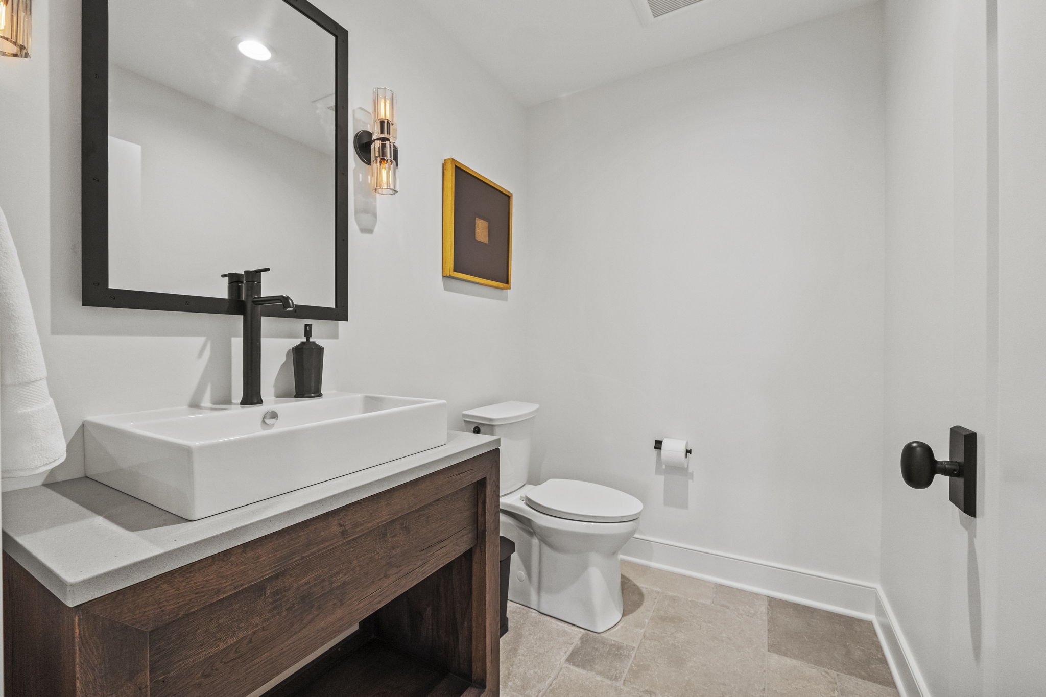 Modern bathroom with a white sink, black faucet, and mirror above, alongside a toilet and a wall-mounted toilet paper holder.