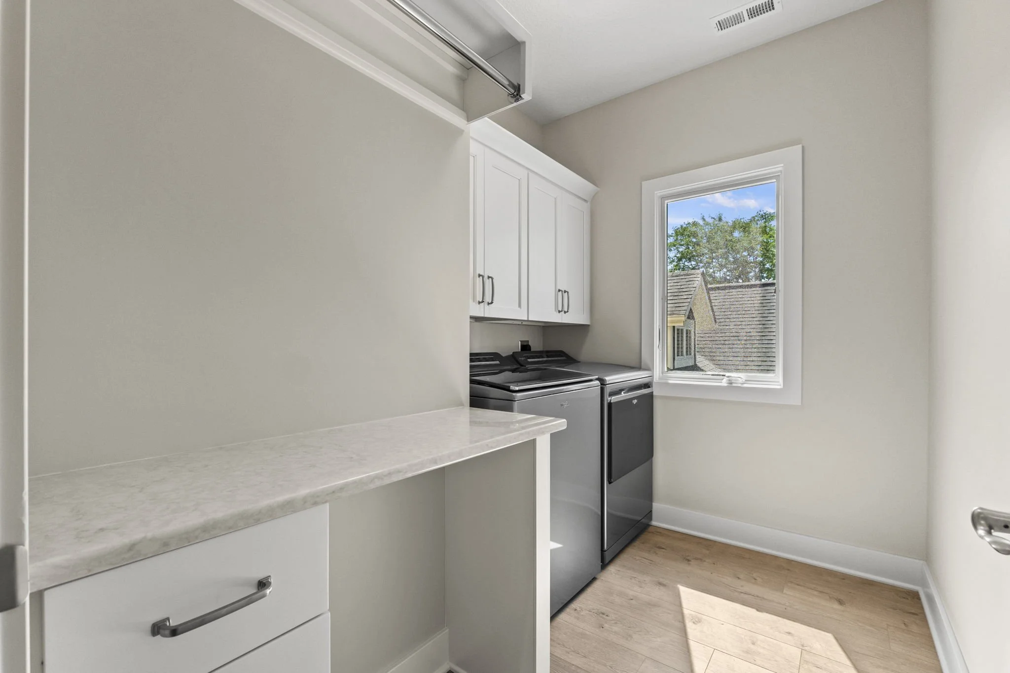Laundry room with white cabinets, a window, and a washing machine and dryer, with a wood floor and natural light.