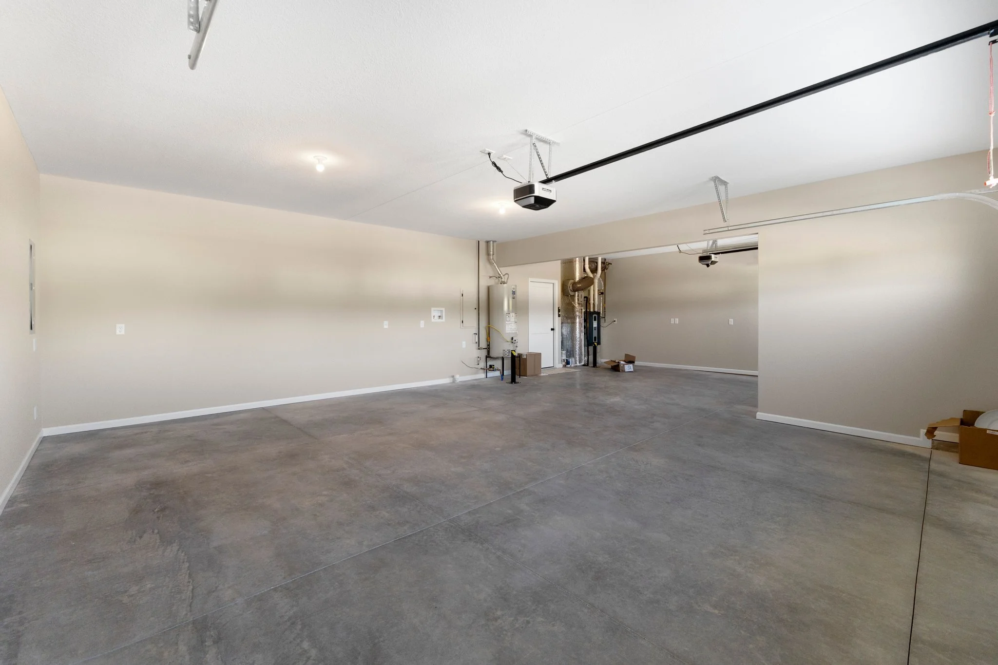 Empty garage with concrete floor, beige walls, and ceiling-mounted garage door openers.