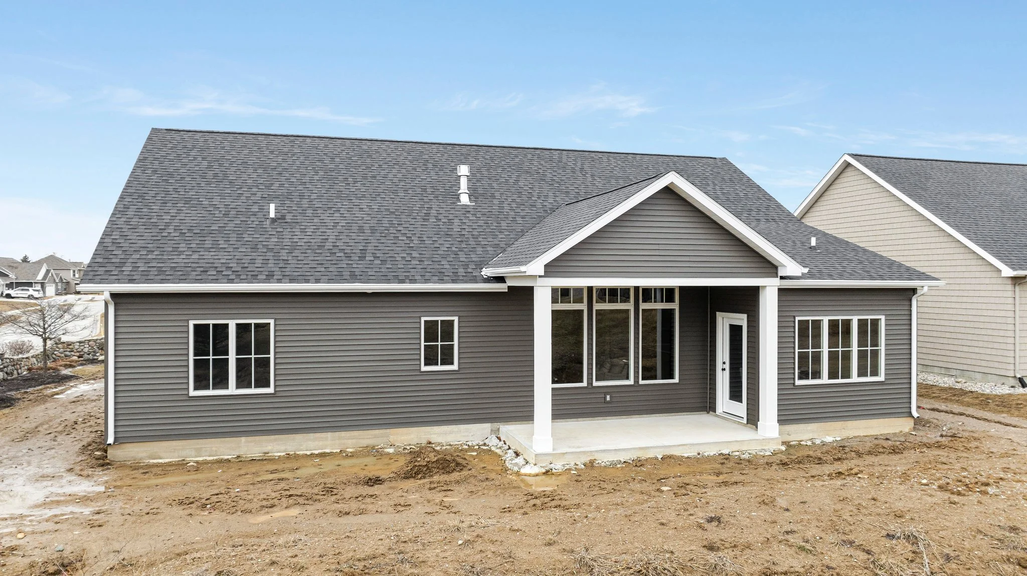 A newly constructed gray house with a sloped roof, large windows, a covered patio, and an unequipped yard.