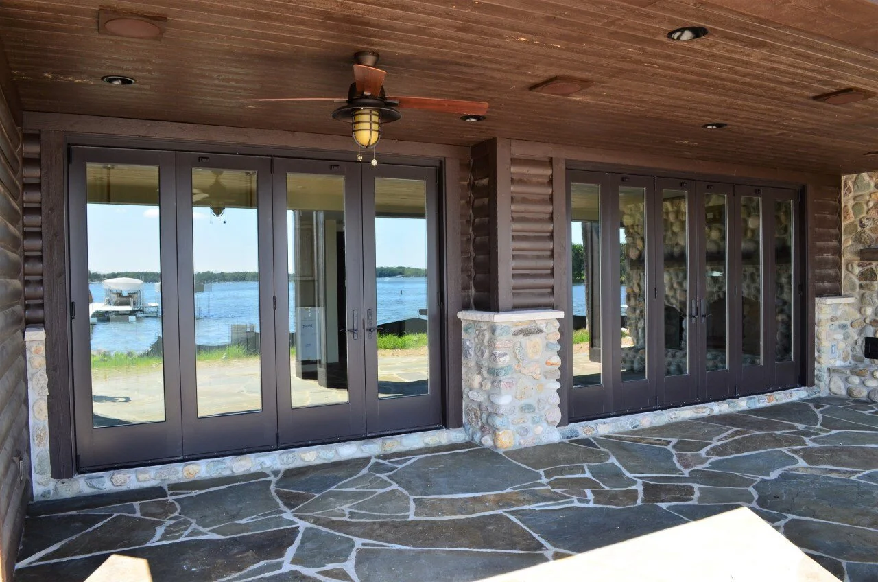 Stone and wood patio area with glass doors leading to a waterfront view, ceiling fan, and recessed lighting.