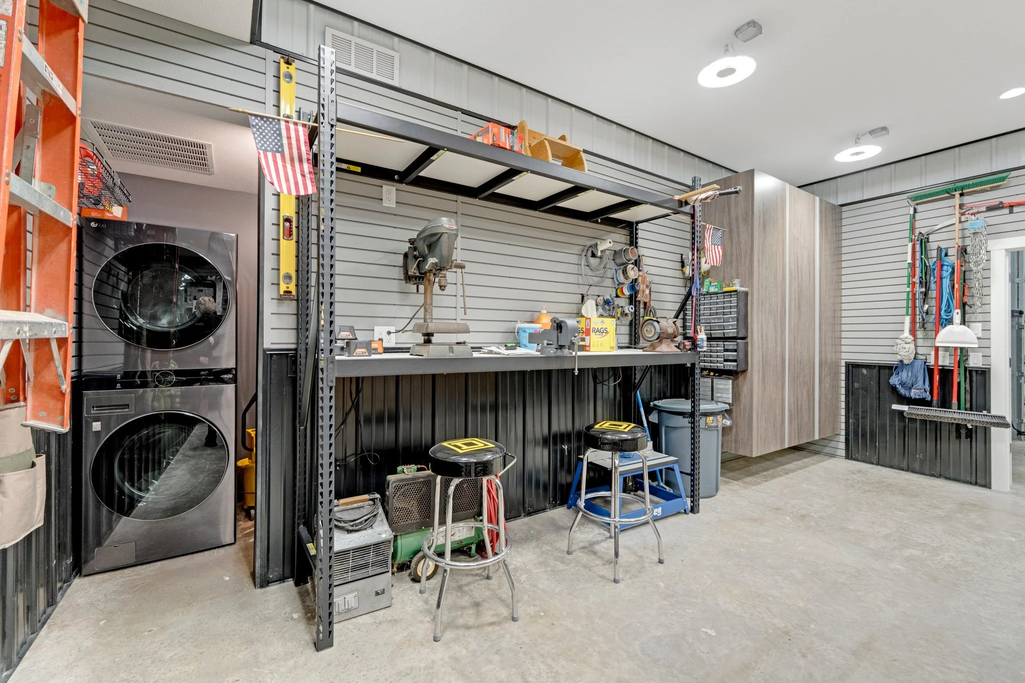 A well-organized garage workshop with a workbench, power tools, shelves, and storage cabinets, including a washing machine and dryer on the left side.