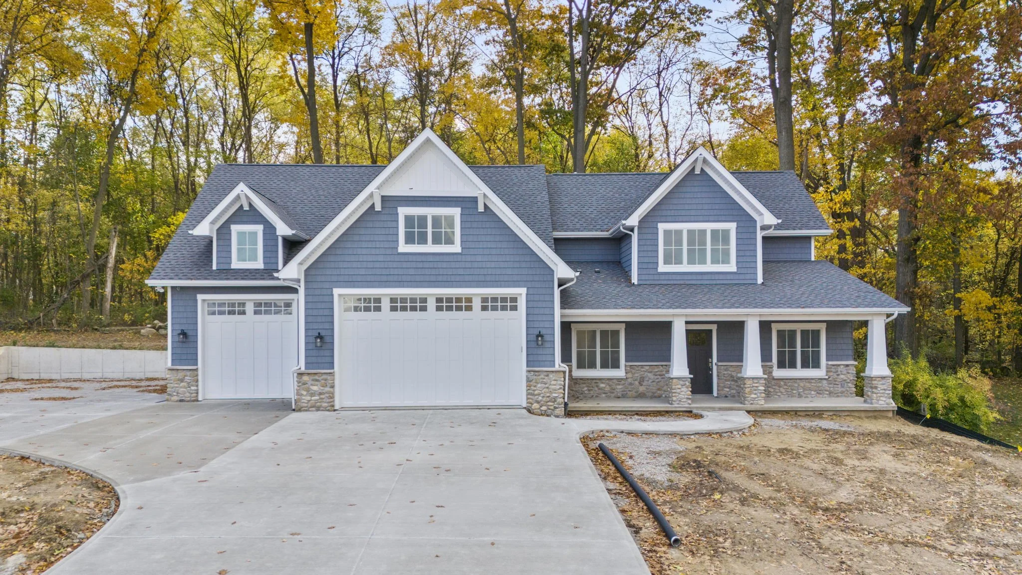 New two-story blue house with white trim, attached garage, stone accents on the front, and surrounded by autumn trees.