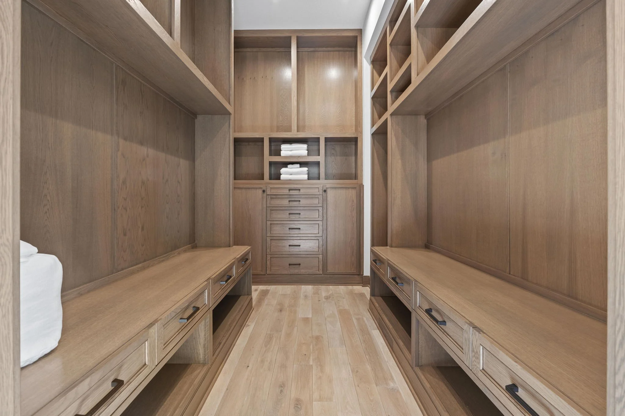 A walk-in closet with wooden shelving and drawers, including towel storage in the middle section.