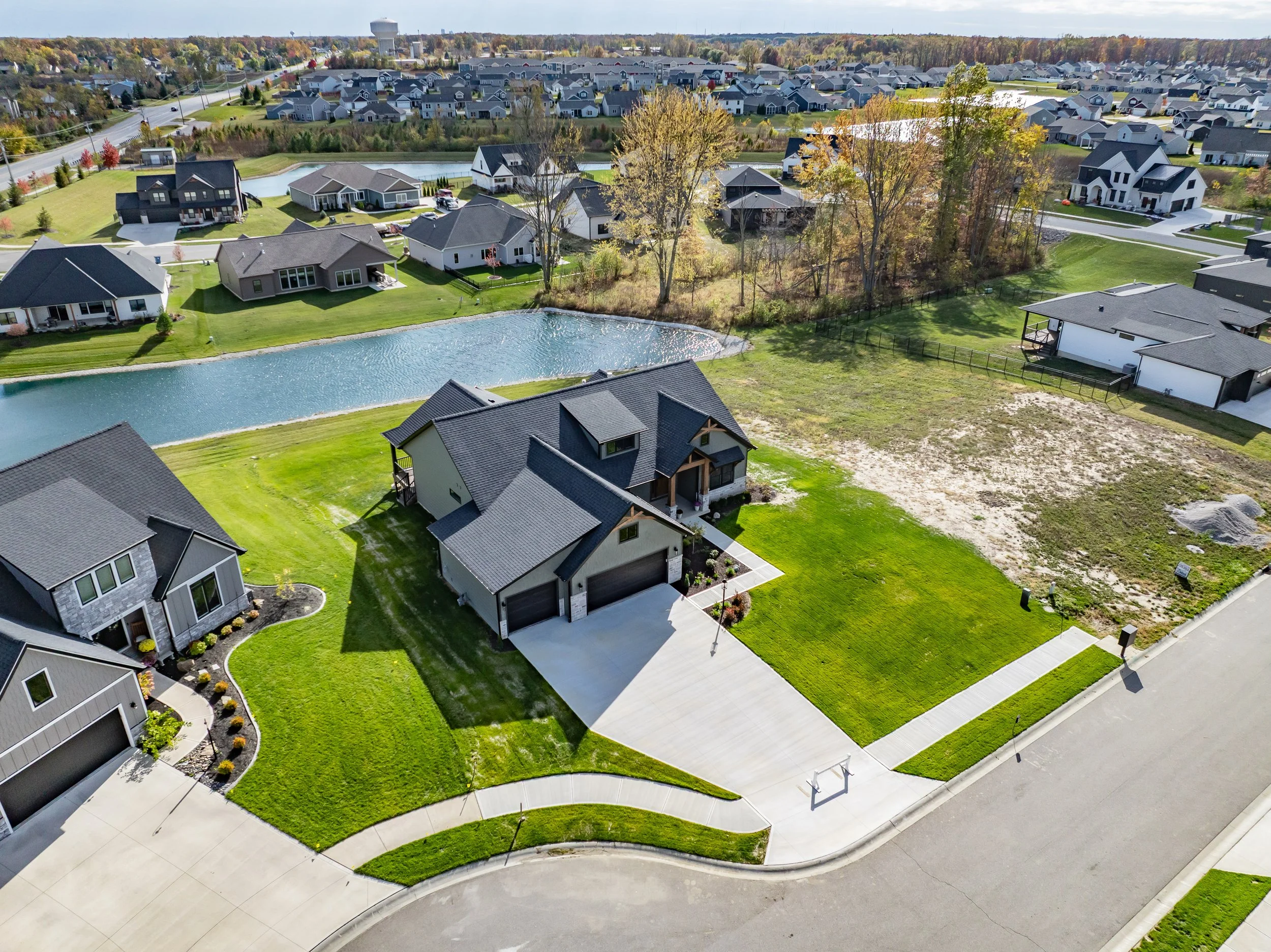 Aerial view of a suburban neighborhood with modern houses, a pond, and green lawns.