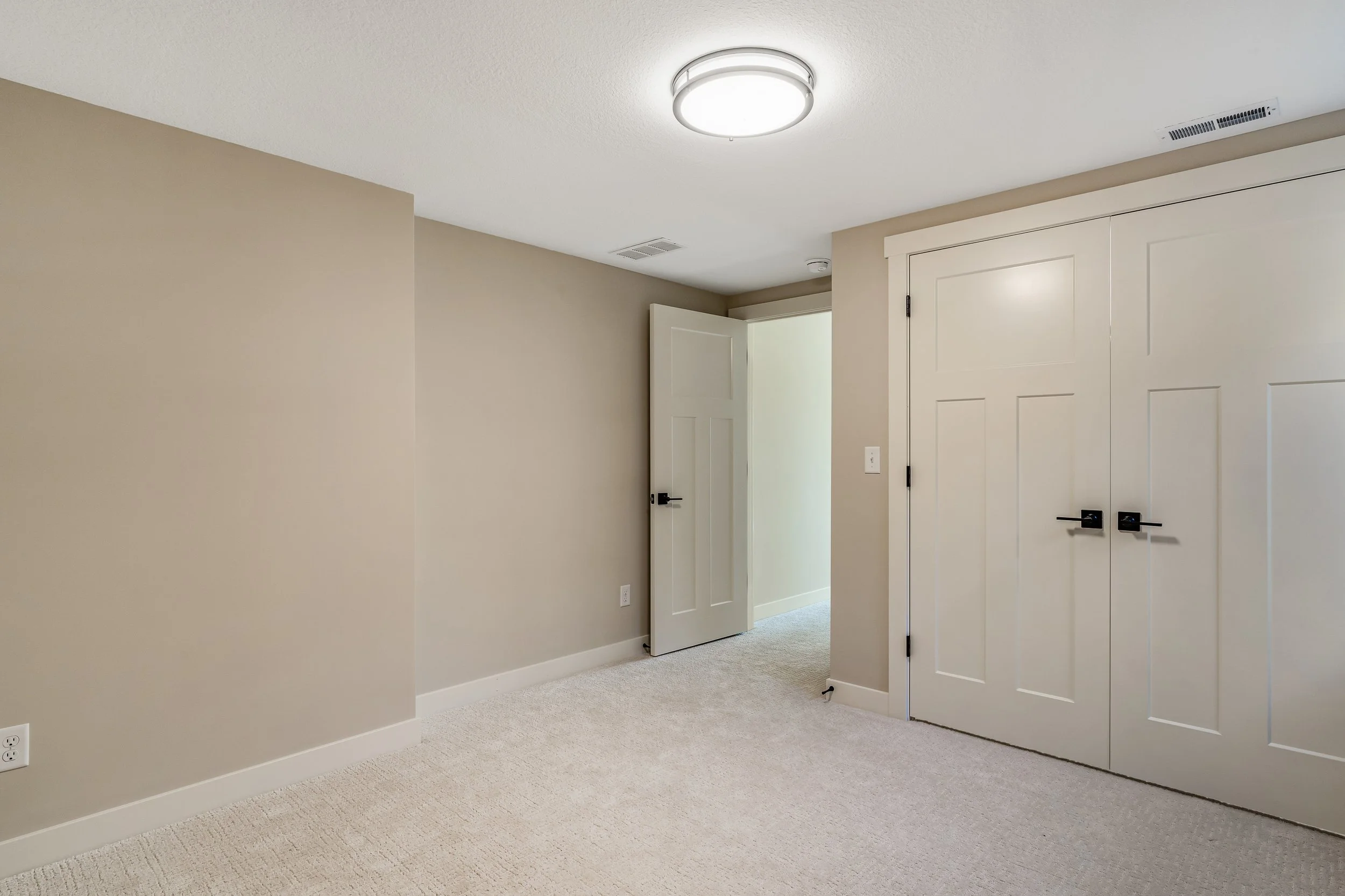 Empty room with beige walls, white carpet, ceiling light fixture, and white closet doors.