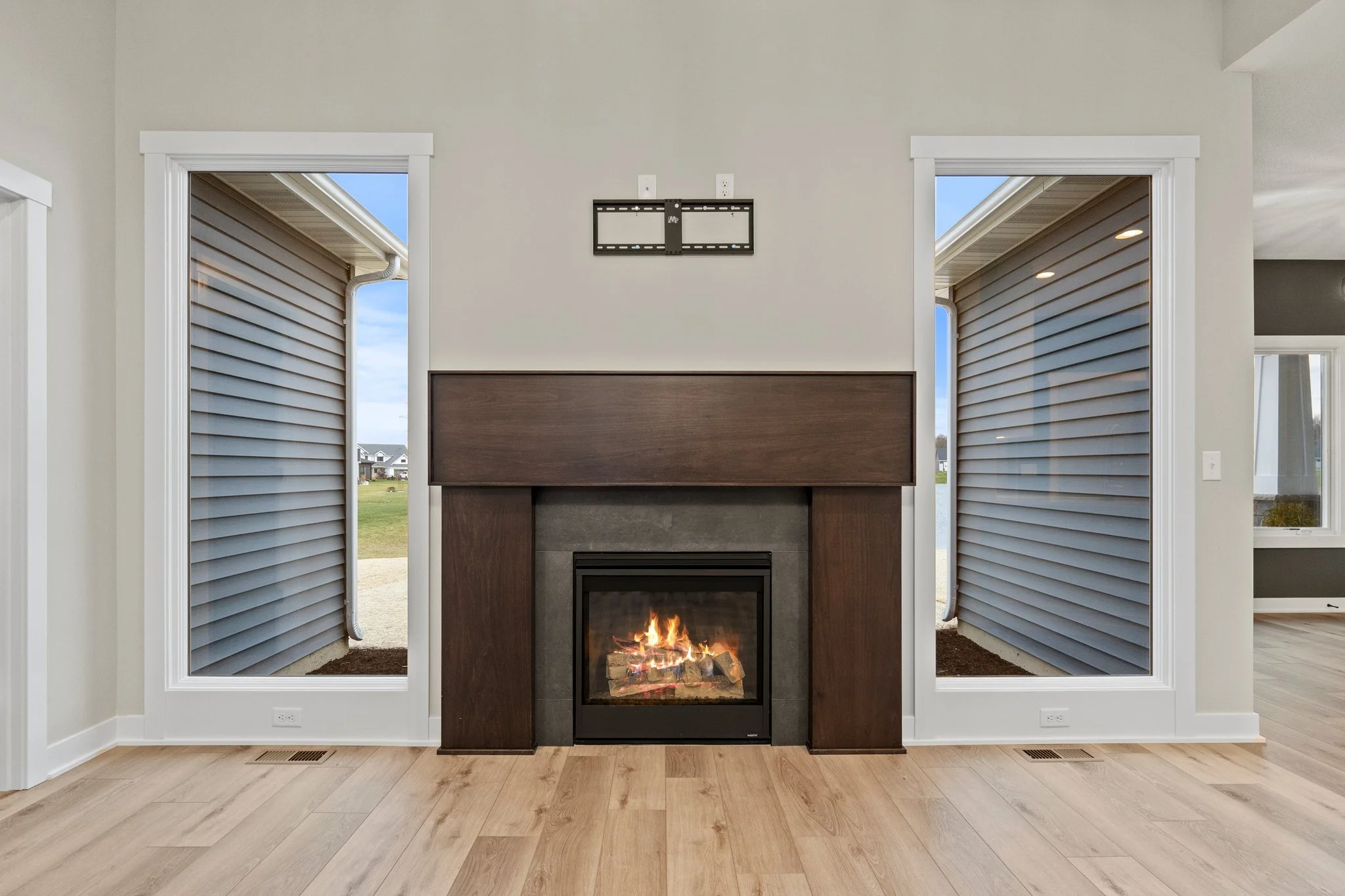 Living room with fireplace, two windows with outside view, wood flooring, and a blank TV mount above the fireplace.