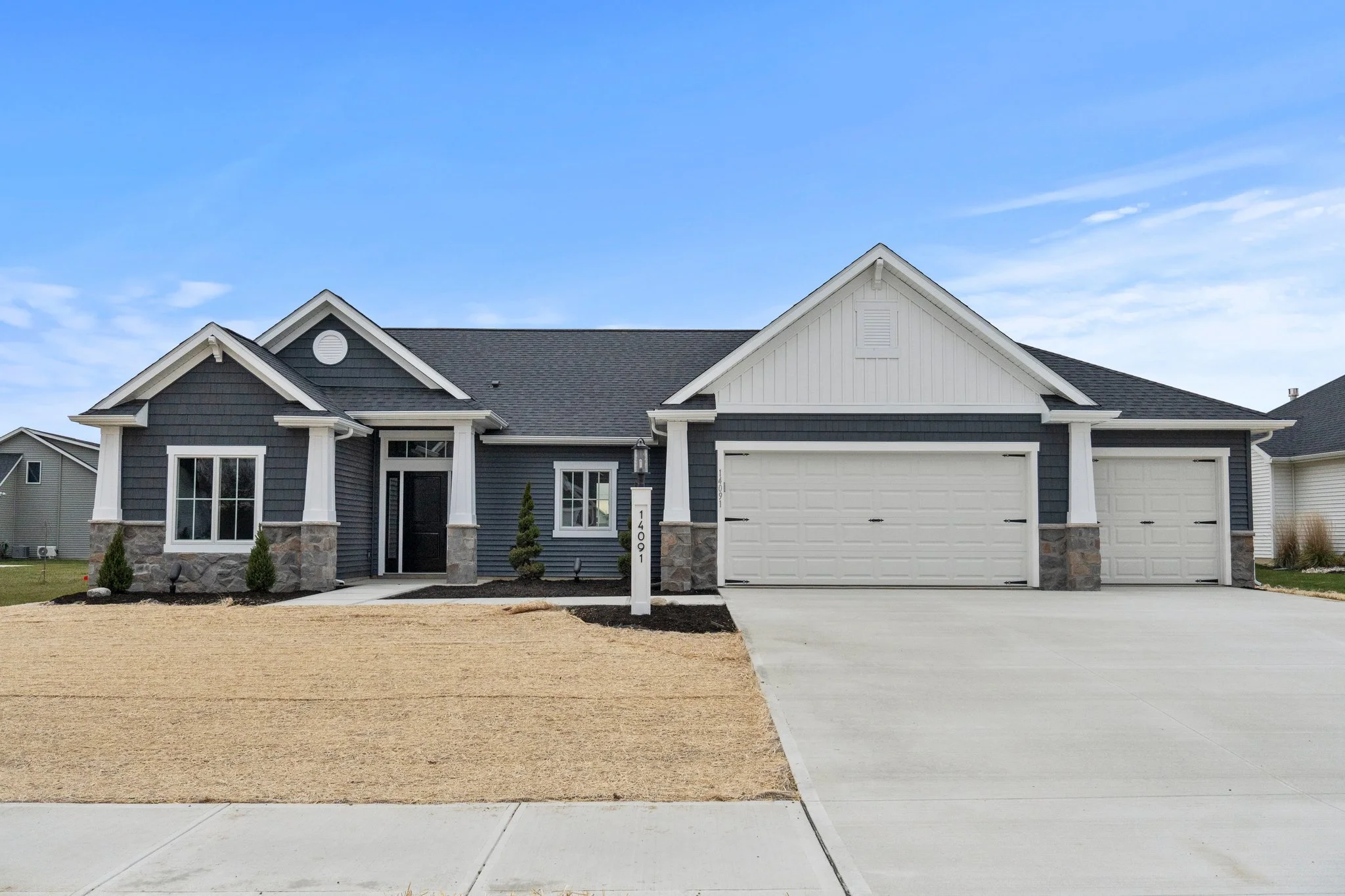 Modern suburban house with dark gray siding, white trim, a stone base, and a three-car garage, on a partly cloudy day.