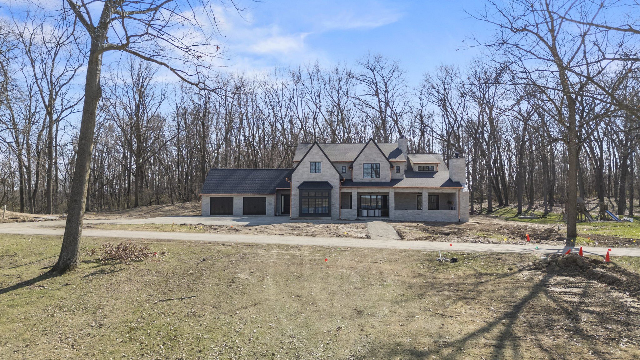 Newly constructed house with a front driveway, surrounded by trees, on a clear day.