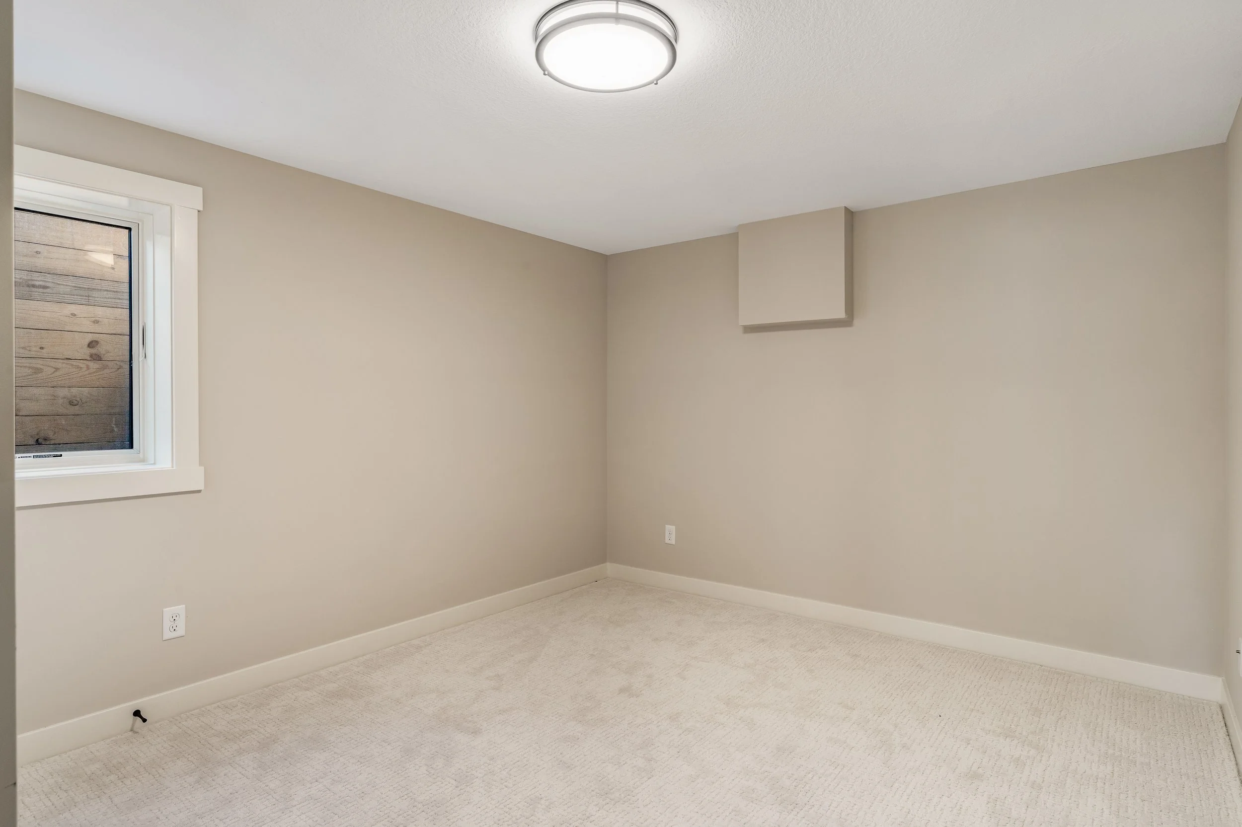 Empty beige room with a window, a ceiling light, and carpeted floor.