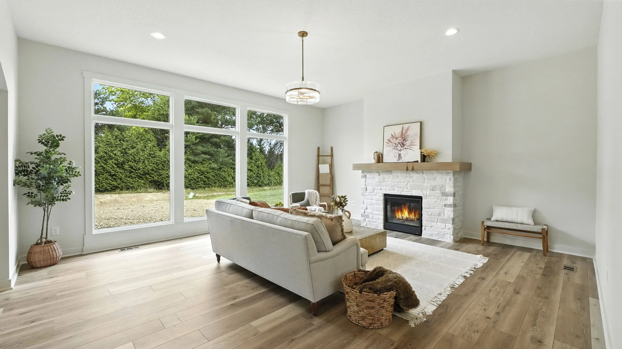 Bright living room with large window, white walls, wooden floor, white brick fireplace, beige sofa, a basket with a furry blanket, and minimal decor.