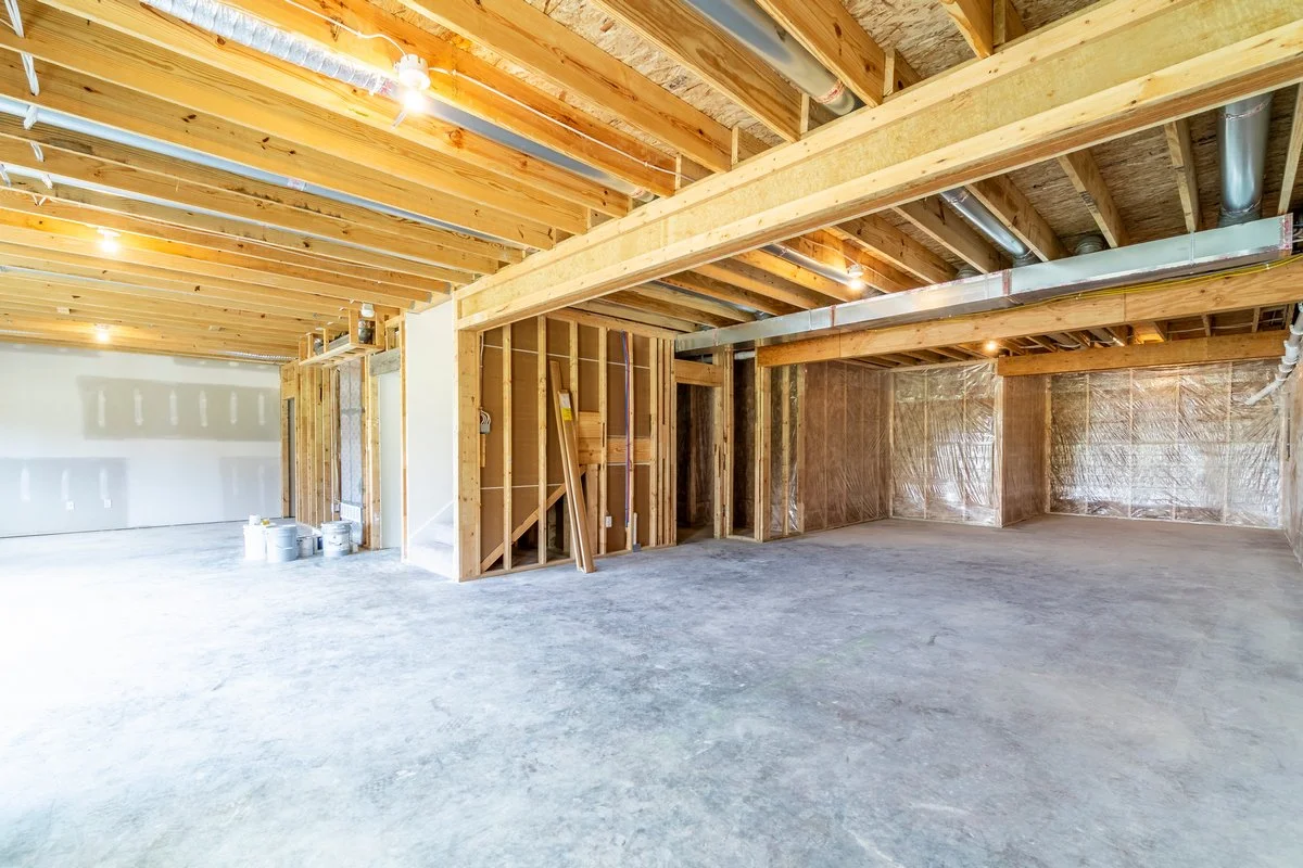 Interior of a building under construction with exposed wooden framework, metal ducts on the ceiling, and a concrete floor.